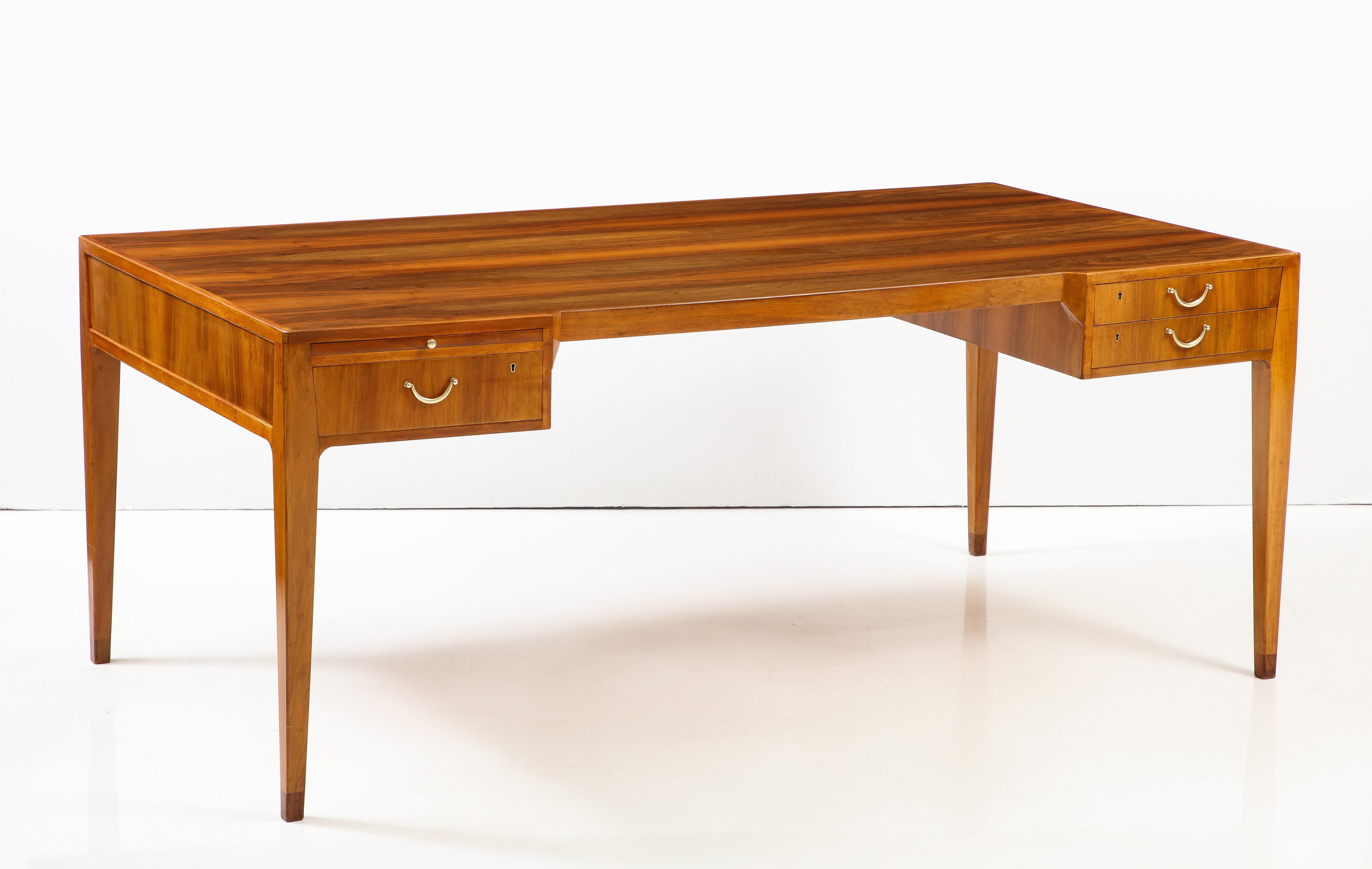A Swedish Modern freestanding writing desk, in striking walnut, Circa 1960s, produced and sold by JKM - Jarnforsens Kontorsmöbler, Stockholm, the rectangular top with long walnut veneers, the sitter edge with a canted front, three short drawers and