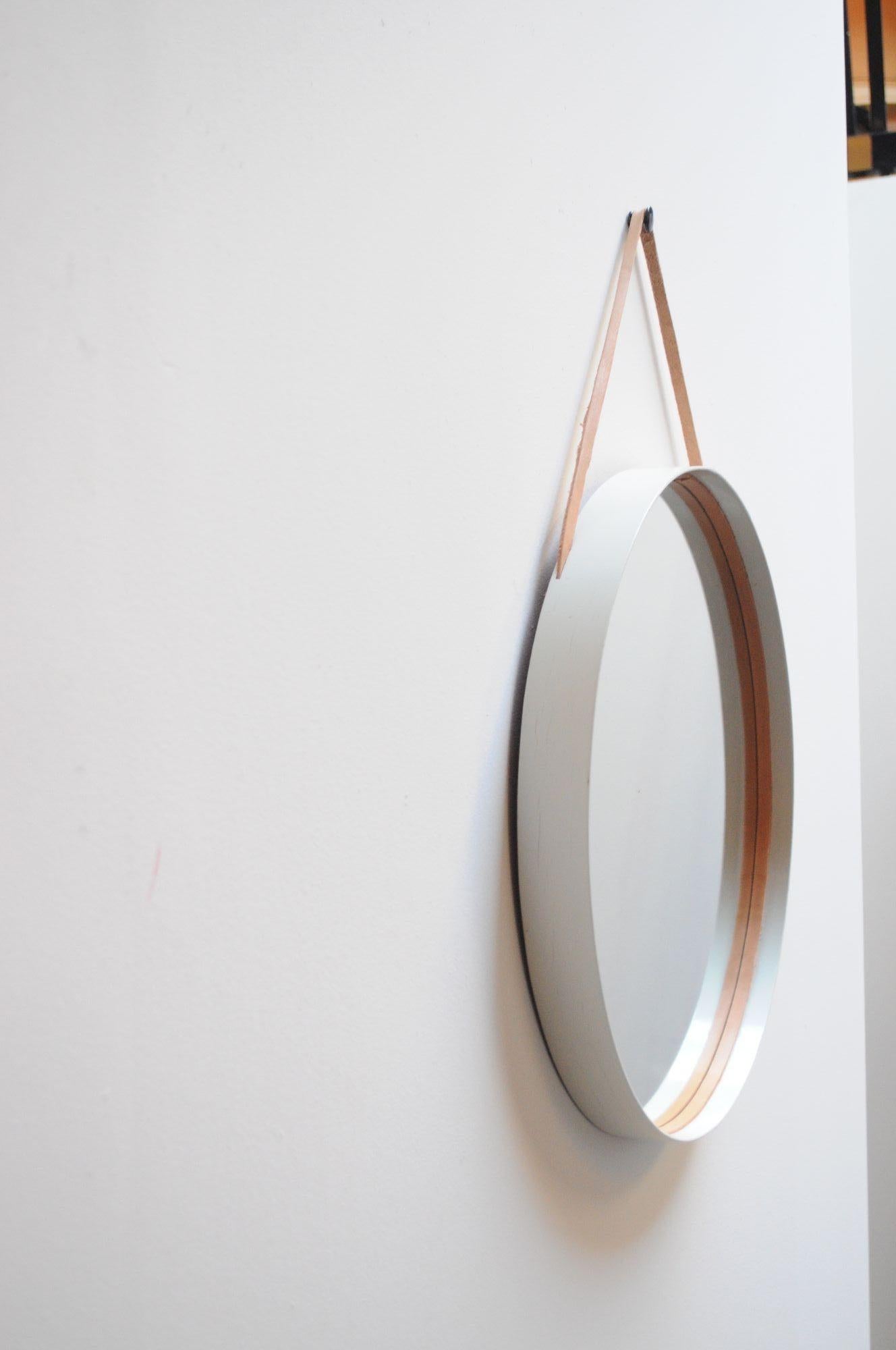 Specchio da parete Glas Mäster con un'insolita finitura bianca (Markaryd, Svezia, anni '60 circa).
È composta da una struttura rotonda in legno curvato con vetro incassato e finiture interne in pelle color corallo chiaro e cinghia (la vernice bianca