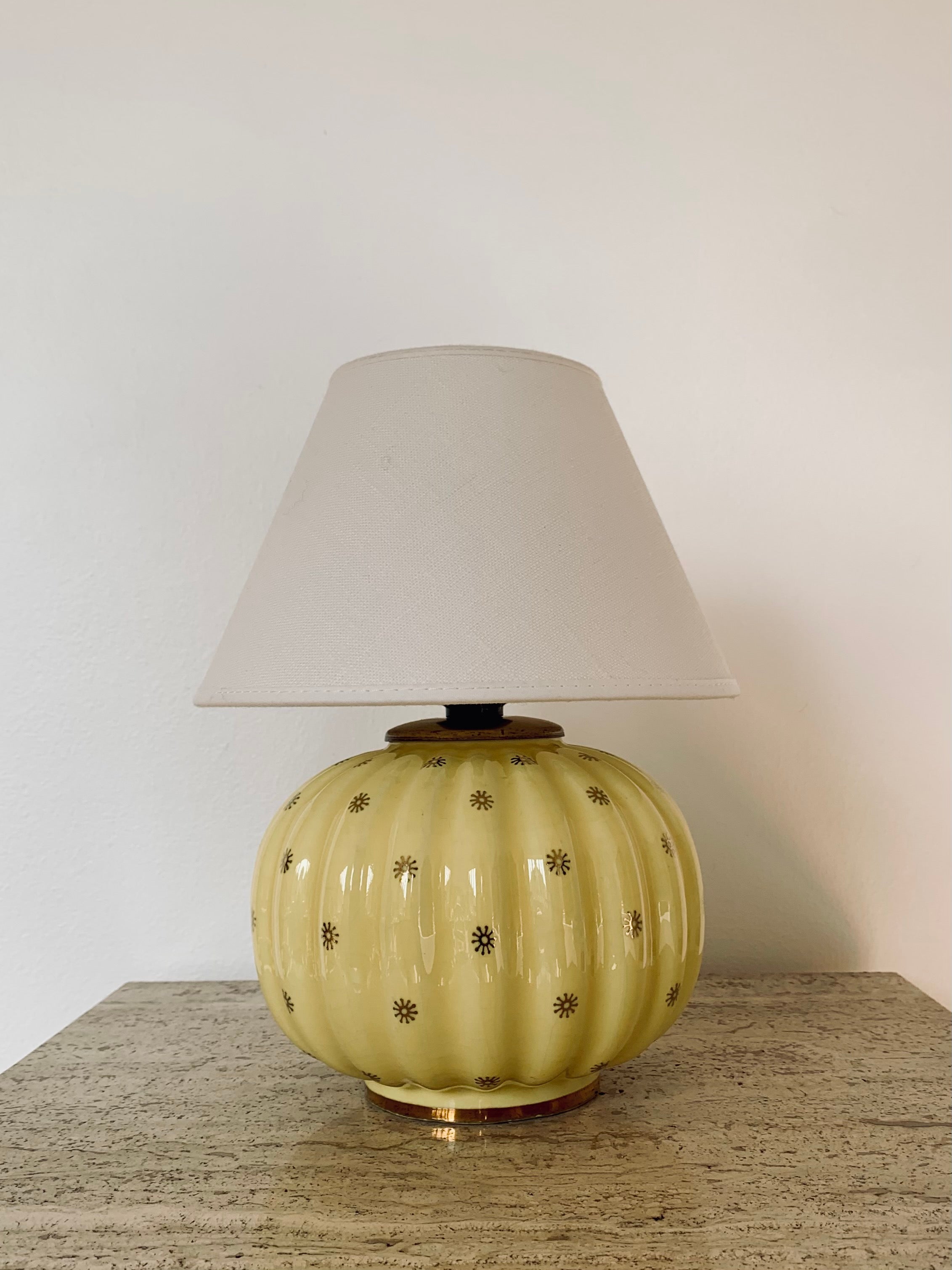 Yellow flint porelain table lamp with gold decor from the 'Neapel' series designed by Arthur Percy for Gefle, Upsala Ekeby, in the 1930s. Round cleft shaped ceramic lampbase with a mild yellow glaze and gilded sun decor. White linnen shade included.