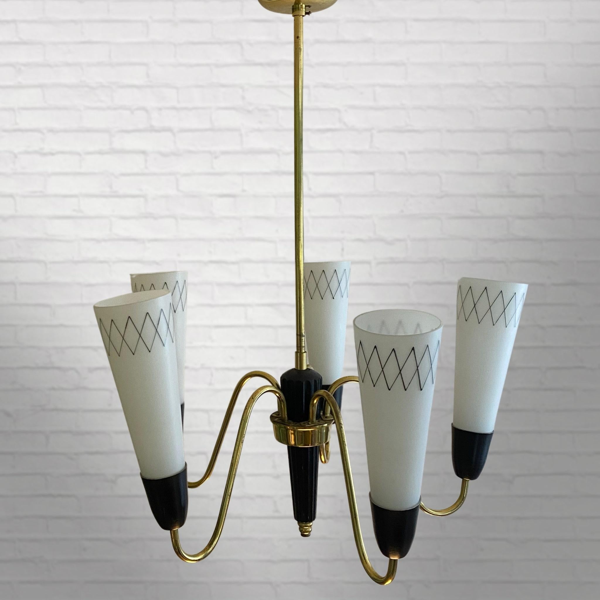 Swedish modernist chandelier made from brass with a black wooden obelisk in the middle. Five curved arms hold cone-shaped glass shades adorned with a geometric pattern. Produced by an unidentified Swedish manufacturer in the 1950s. With its