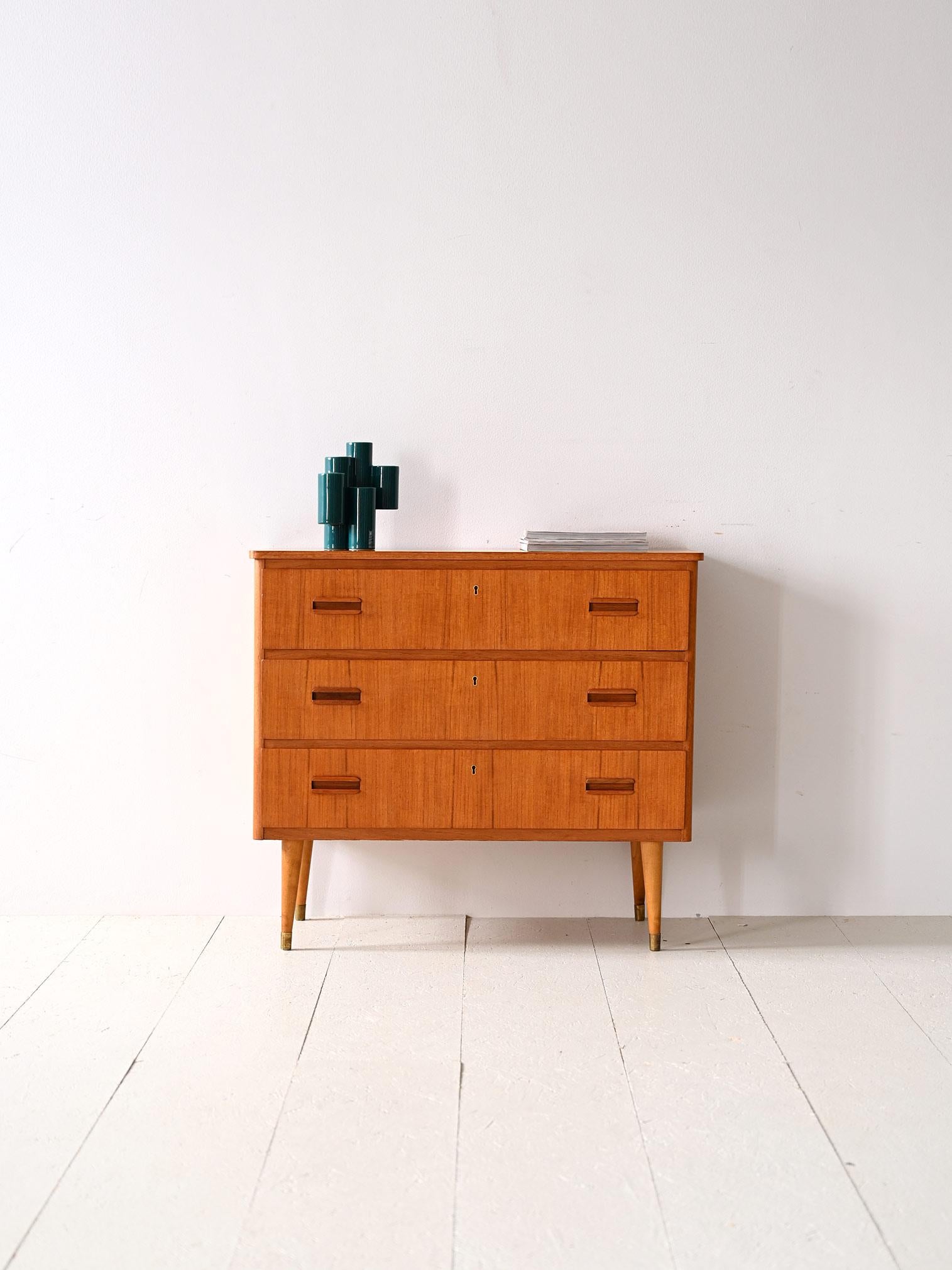 Scandinavian 1960s cabinet with three drawers.

A piece of furniture with modern lines and refined details that is distinguished by the distinctive shape of the drawer handles and the presence of brass ferrules. 
The teak frame consists of three