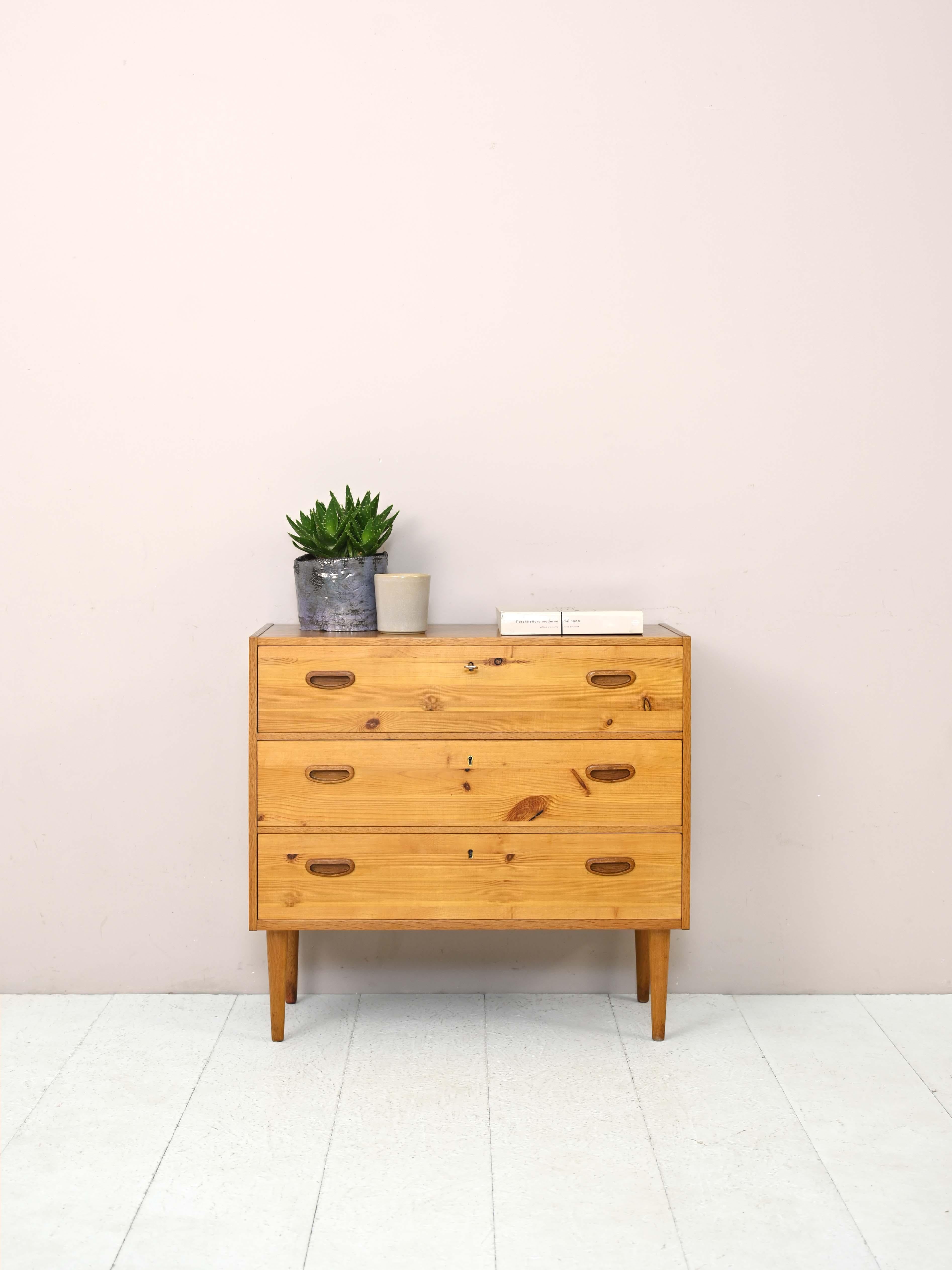 Vintage teak and pine chest of drawers.

A modern piece of furniture that is distinguished by its pine wood drawers characterized by pronounced grain. The rest of the frame is teak wood as is the carved handle of the drawers.
The tapered legs are