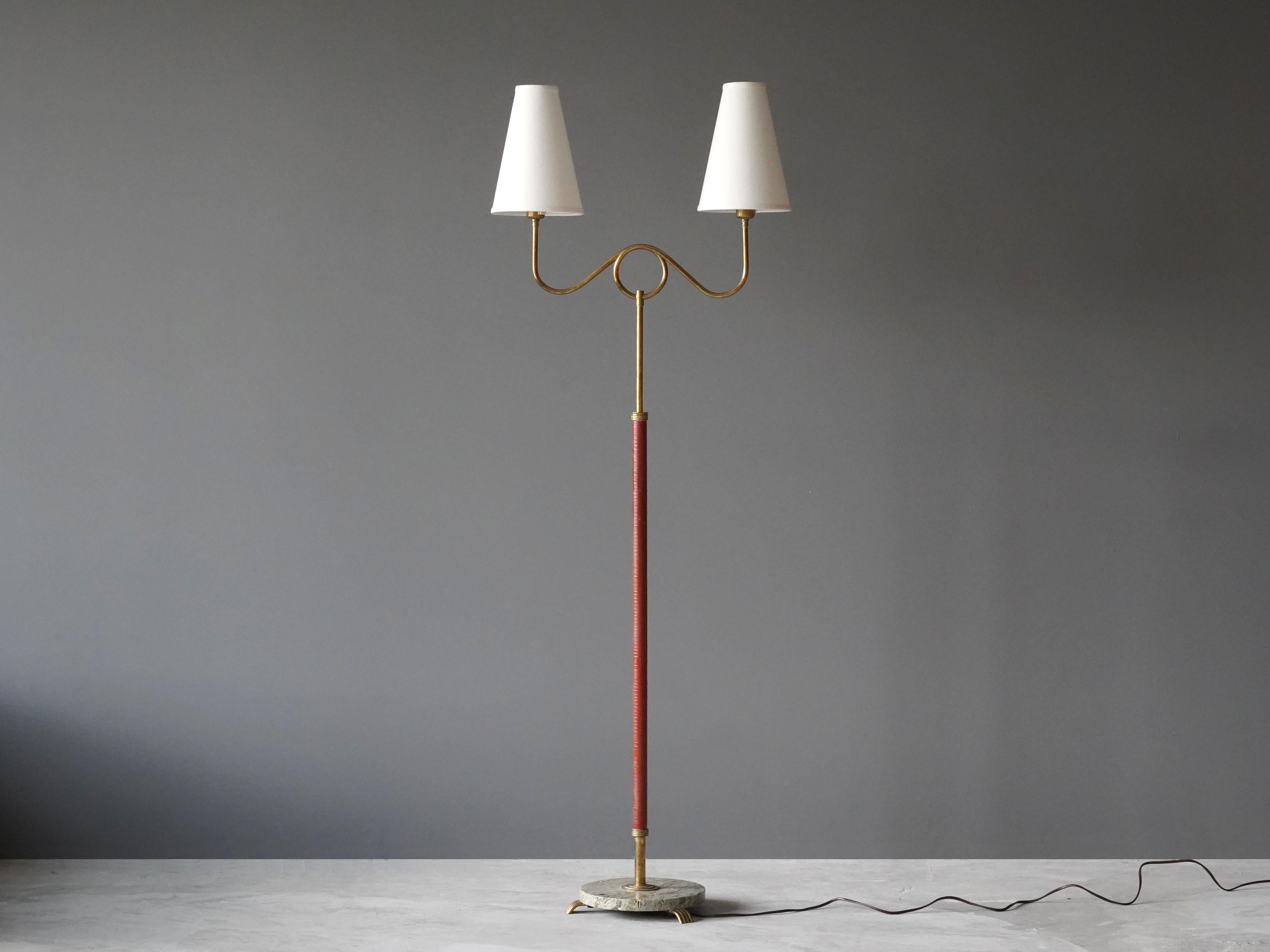A two armed floor lamp by an unknown Swedish modernist designer. Produced in Sweden, 1940s. In brass, original red leather, on a brass base. 

Other designers of modern lighting with a similar organic expression include Paavo Tynell, Josef Frank,