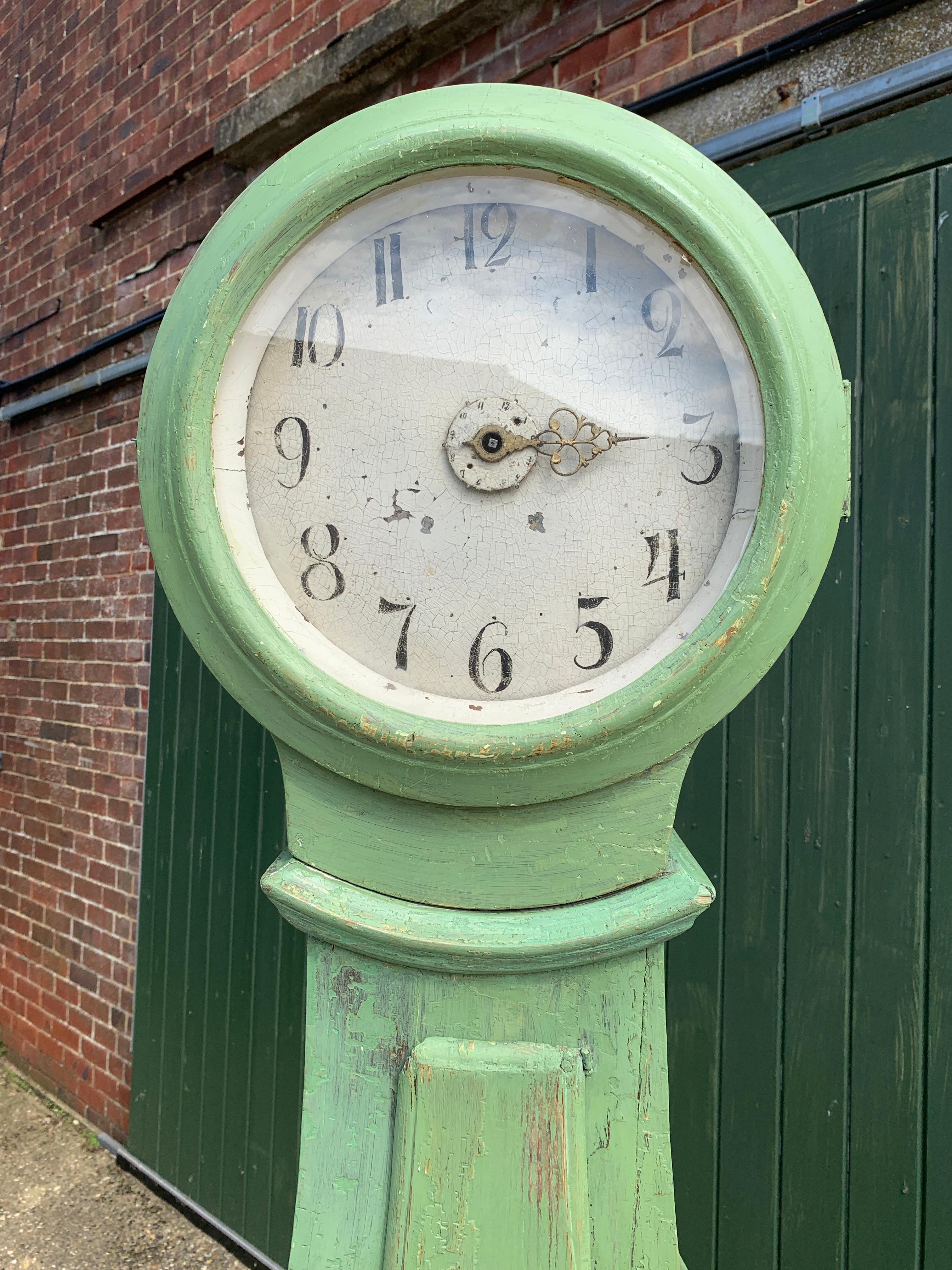 Beautiful early 1800s antique Swedish mora clock with unusual oversize hood and larger face and highly carved body in later paint 
Measures: 206cm.

The clock body is distressed as befits its age and has the usual wood movement found in clocks of