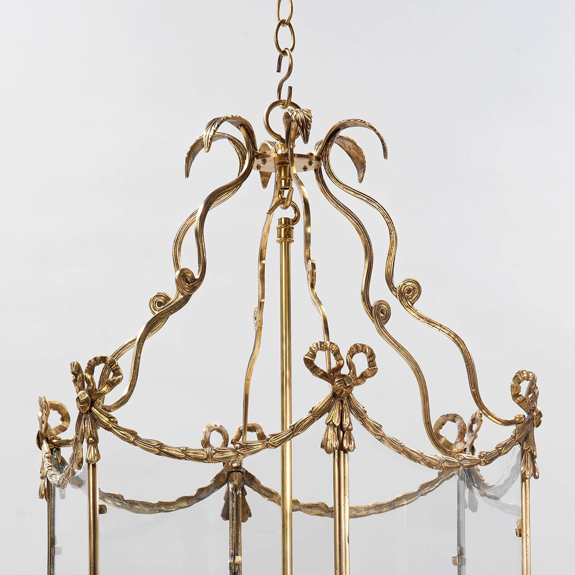 The Swedish neoclassic style three-light brass hall lantern with 18th century style embellishments. The leaf tip crown above scrolling supports and a hexagonal frame decorated with bowknots, tassels, and bellflower swags. The base decorated with