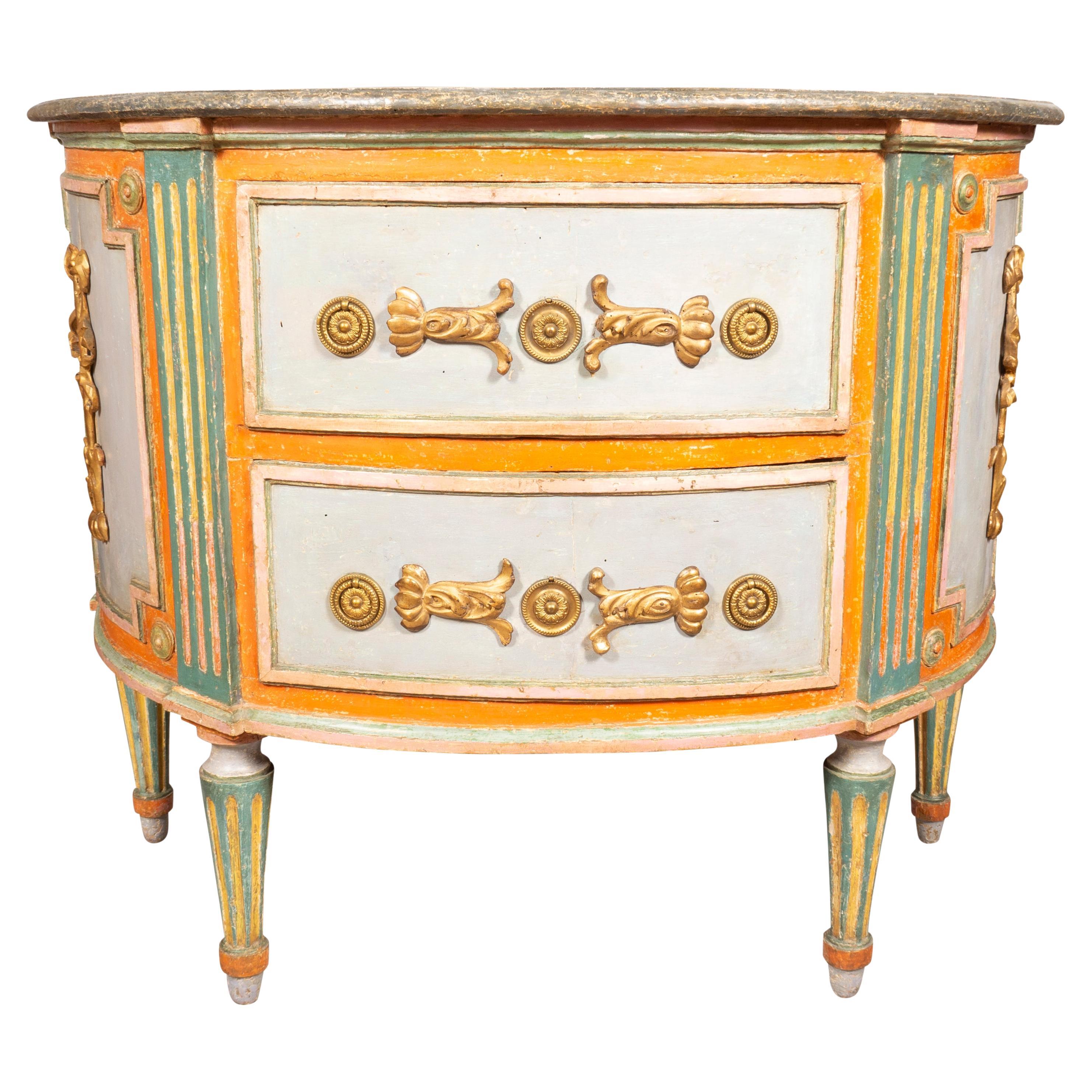 With demilune white and grey faux marble top over a conforming case section with two drawers with brass ring handles and stylized mounted giltwood acanthus leaves ,the case sides with gilded ribbon tassels. Raised on circular tapered fluted legs.