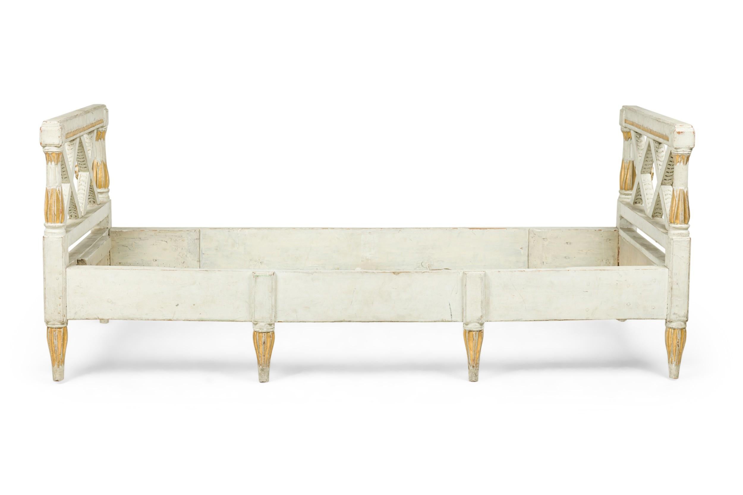 Swedish Neo-Classic (18/19th Century) white painted and gilt trimmed daybed with with carved open double X design side arms with a singe beige and green patterned upholstered cushion and resting on tapered shaped fluted legs
 

 Condition: painted
