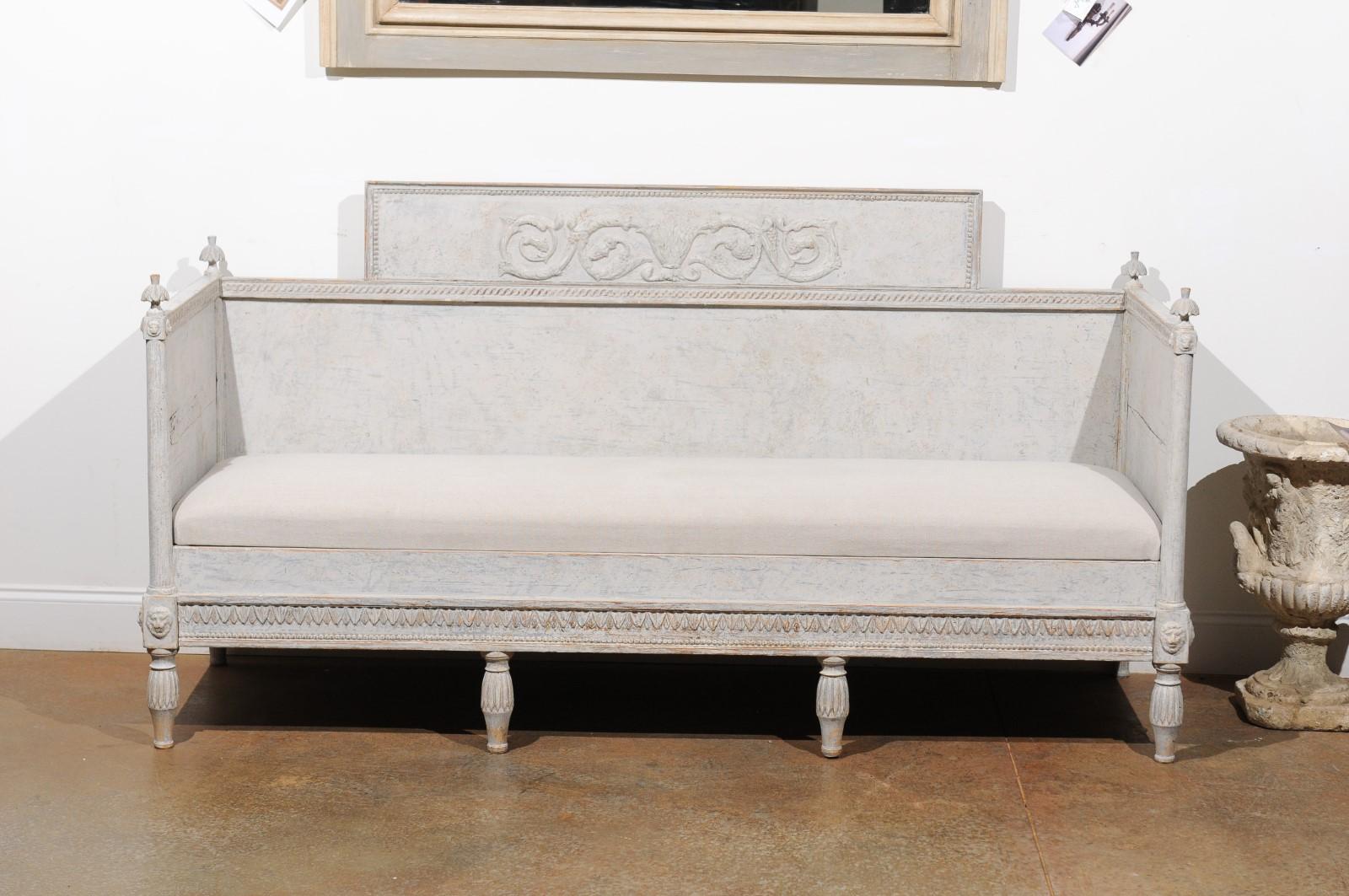 A Swedish neoclassical painted wood sofa bench from the early 19th century, with scrollwork design, lions, beads, waterleaf motifs and new upholstery. Born in the early years of the 19th century during the Gustavian era, this exquisite painted sofa