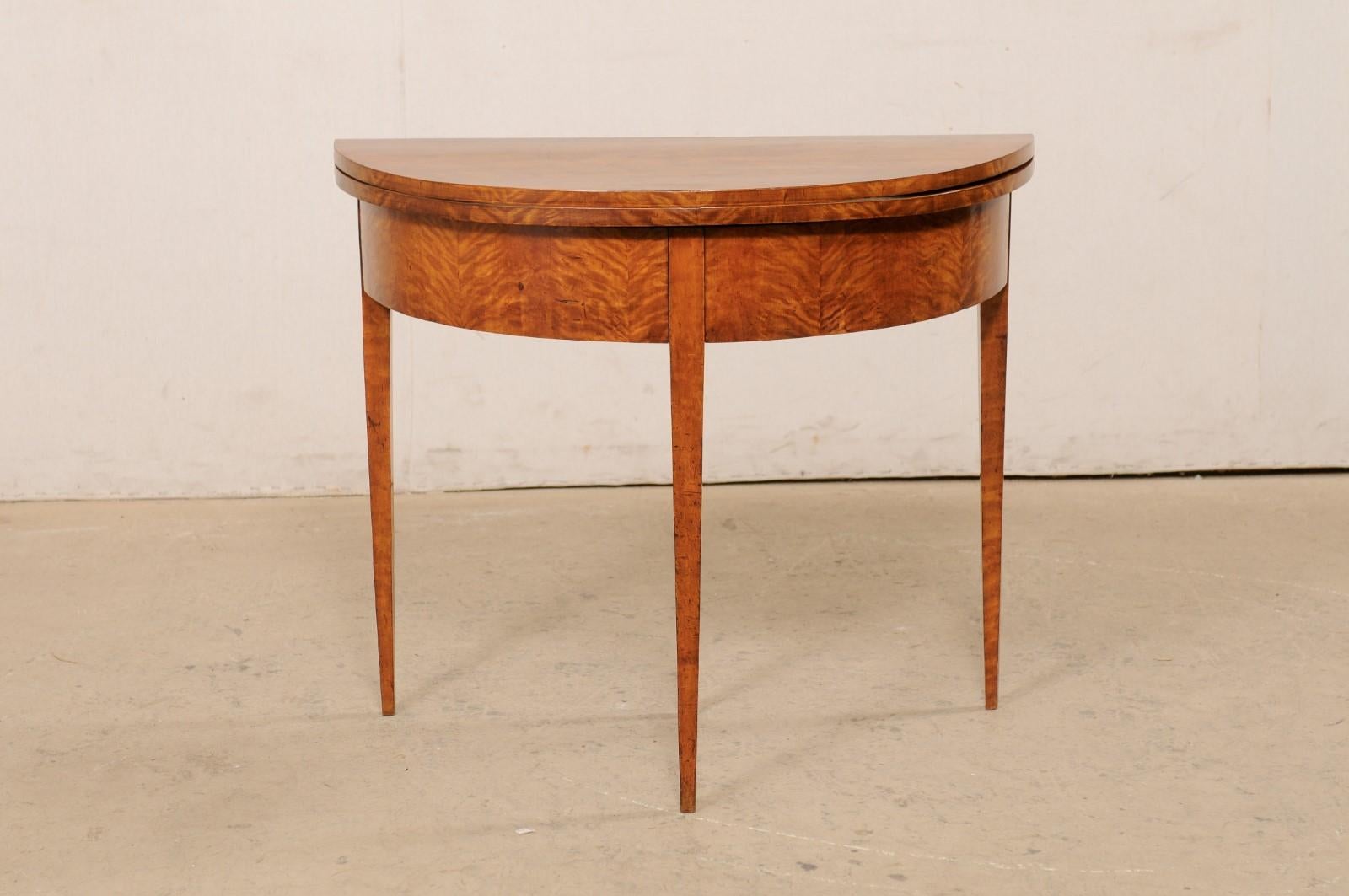 A Swedish Neoclassical style demi-lune table, which converts to a round table, circa 1820's. This antique table from Sweden features a half moon top over a smooth/rounded apron, and is raised upon squared legs, that gently taper towards their feet.