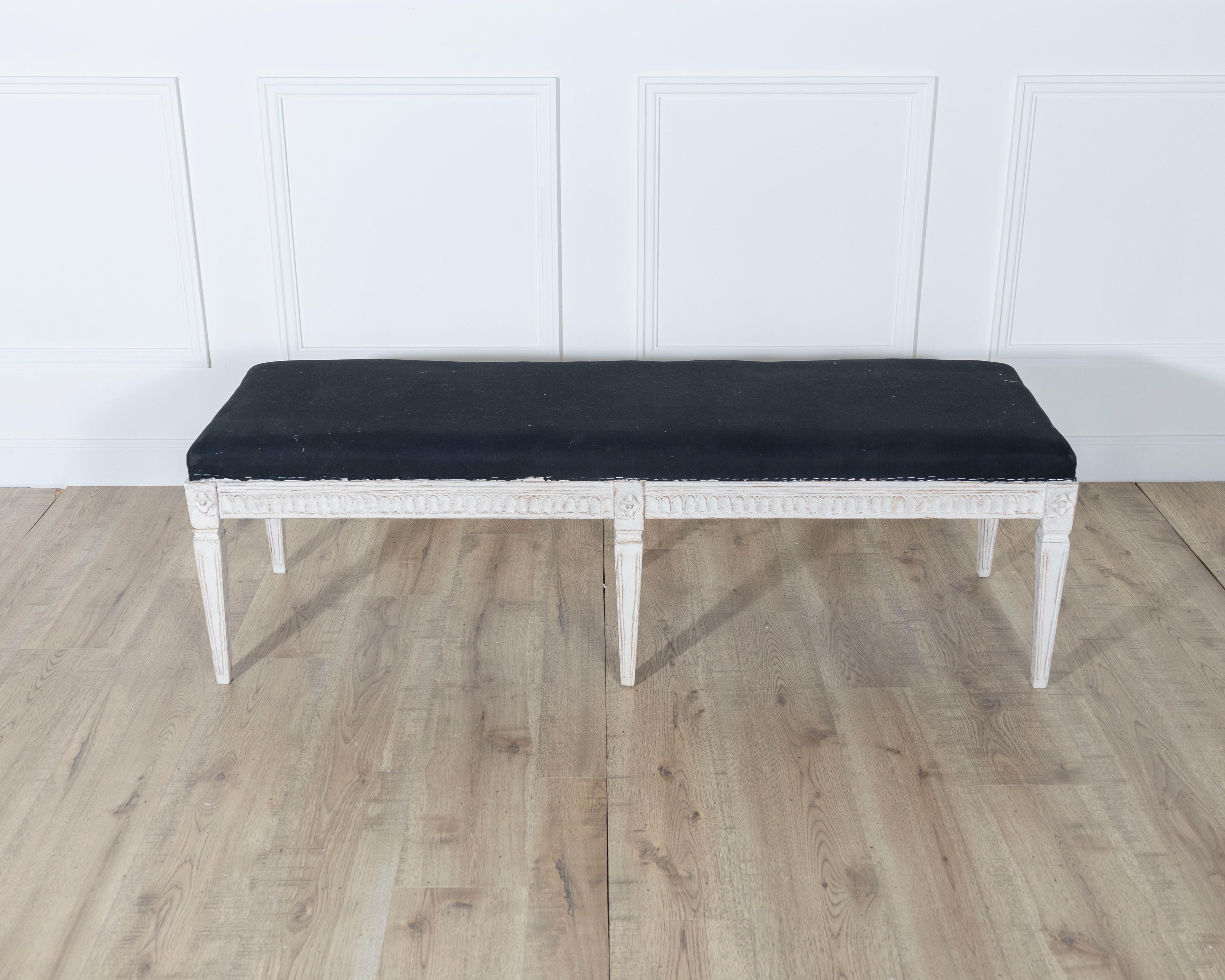 A refined Swedish bench dating to circa 1880, embodying the graceful elegance of the Neoclassical style. The frame is delicately carved and retains traces of its original painted finish, a soft white that has acquired a beautiful patina over time.