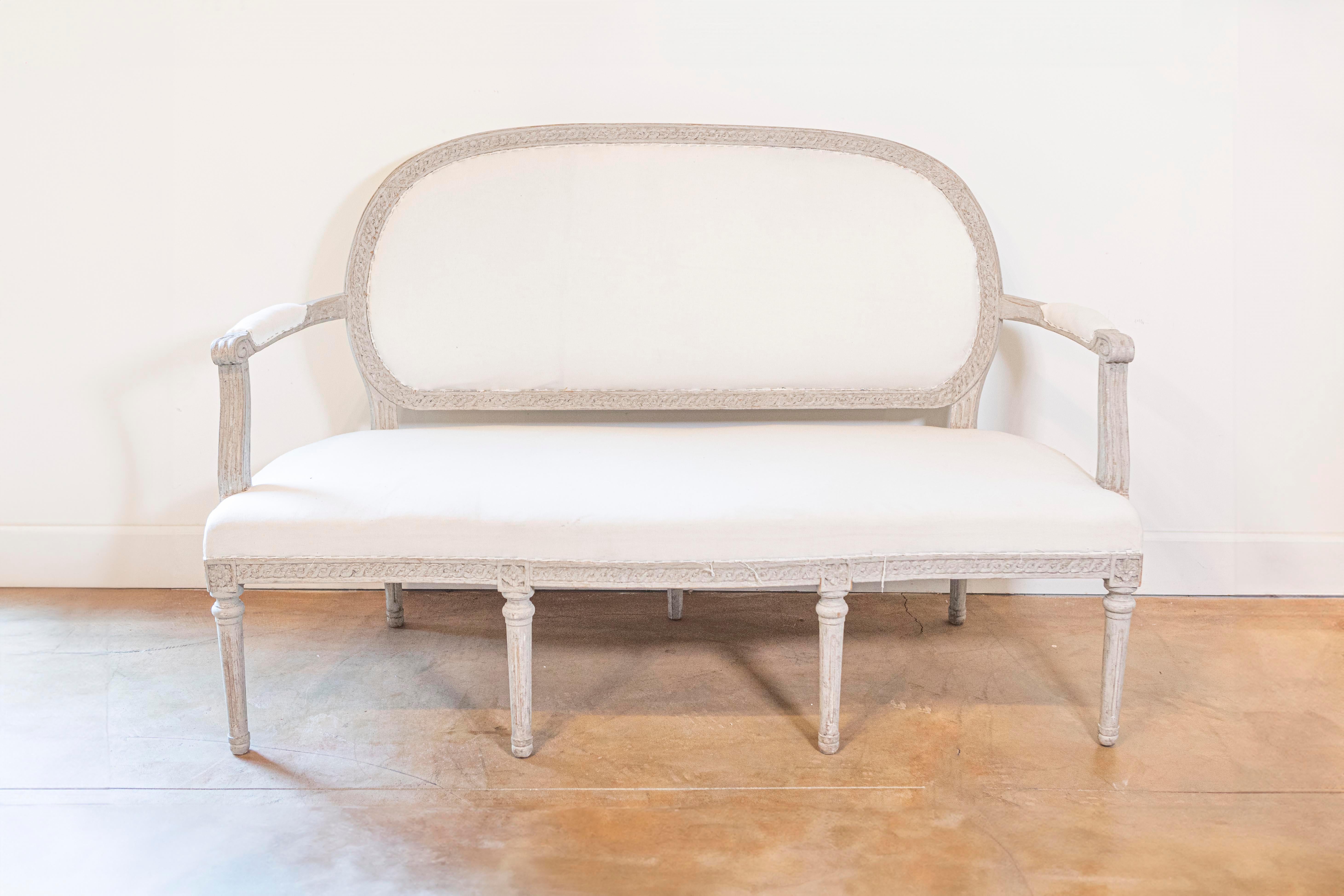 Divano in legno dipinto di epoca neoclassica svedese del 1780 circa con schienale ovale, fregio arabescato intagliato, braccioli a voluta, sette gambe e rosette intagliate. Celebra l'eleganza classica con questo squisito divano in legno dipinto di