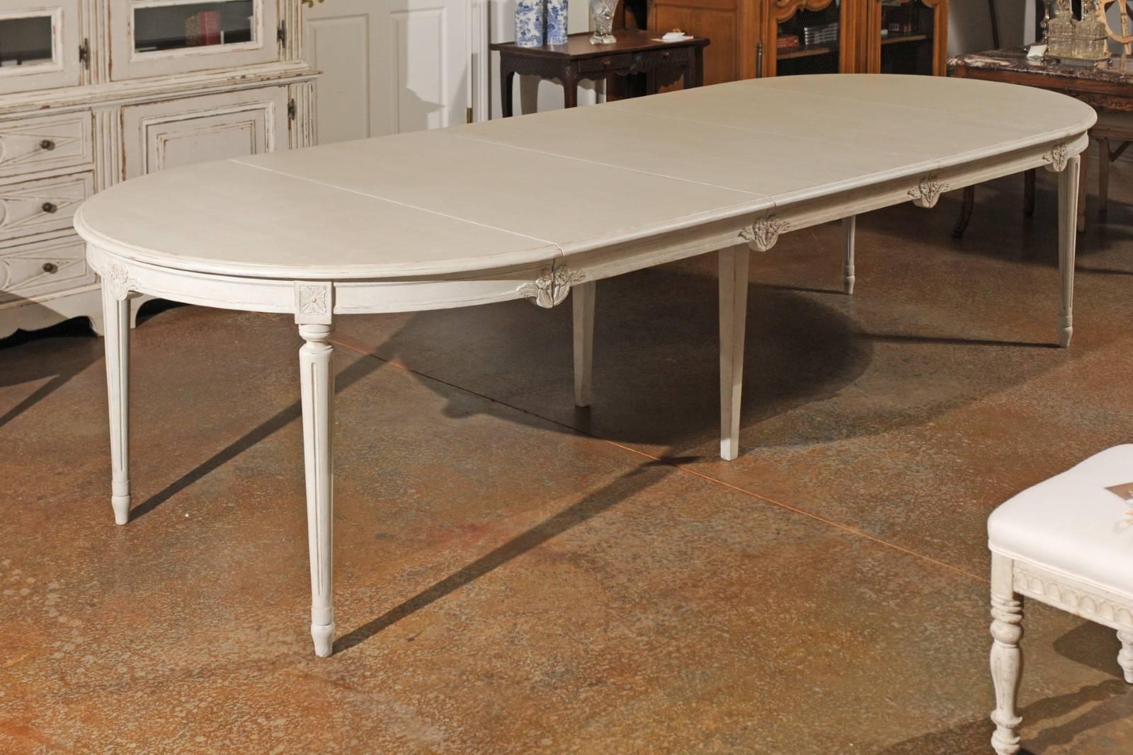A Swedish oval neoclassical style painted extension dining room table from the early 20th century with three leaves and fluted legs. This exquisite Swedish long dining room table features an oval top, comprising three removable leaves that extend
