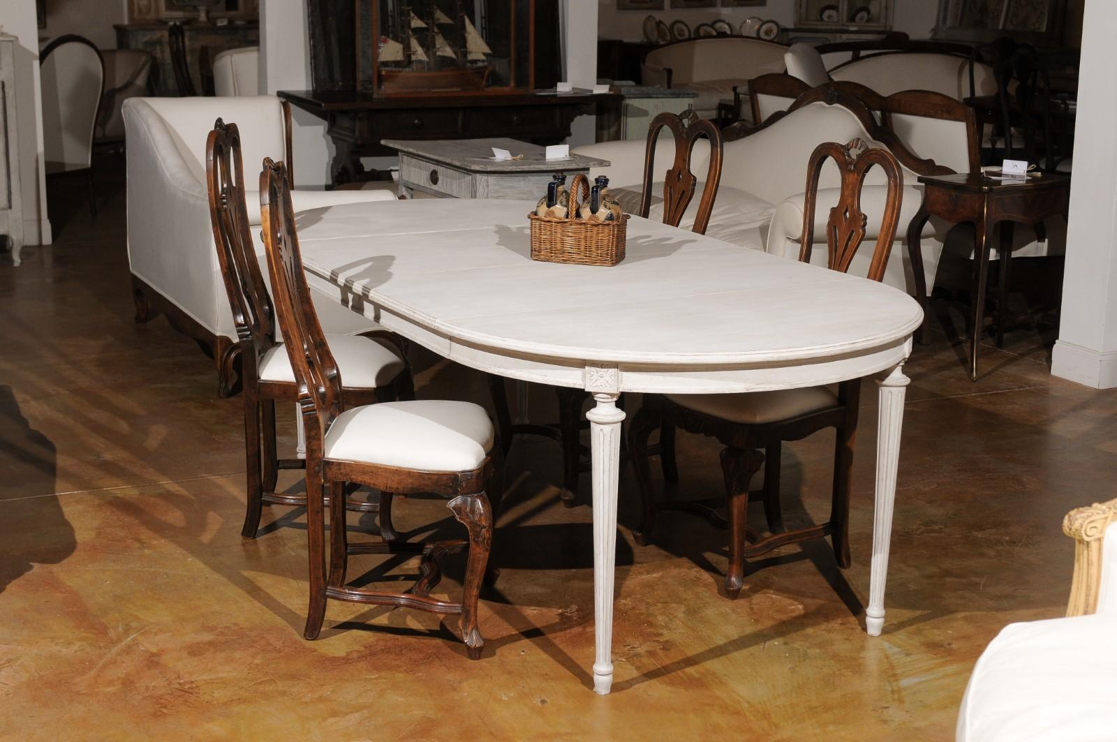 A Swedish neoclassical style painted wood oval extension dining table from the 19th century with two leaves and fluted legs. Born in Sweden during the 19th century, this dining table features an elegant top that opens up to receive two additional
