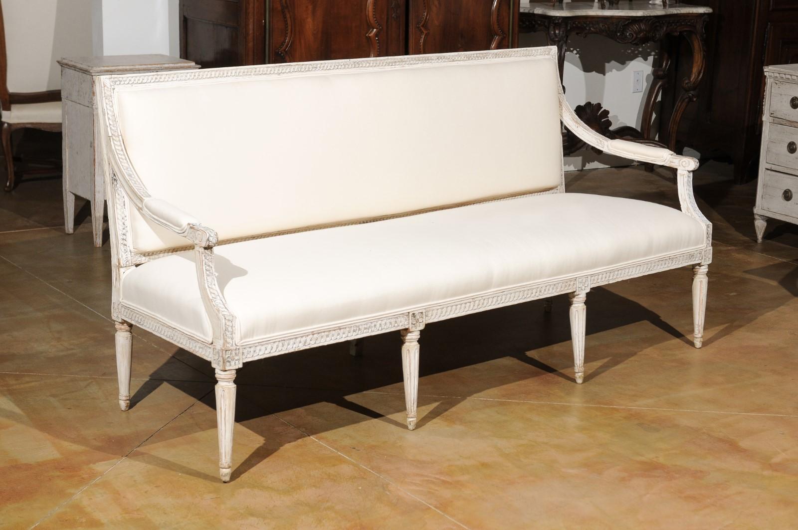 A Swedish Neoclassical style painted wood sofa from the 19th century, with scrolled arms, guilloche motifs, fluted legs and new upholstery. Born in Sweden during the 19th century, this elegant sofa features a rectangular back adorned with guilloche