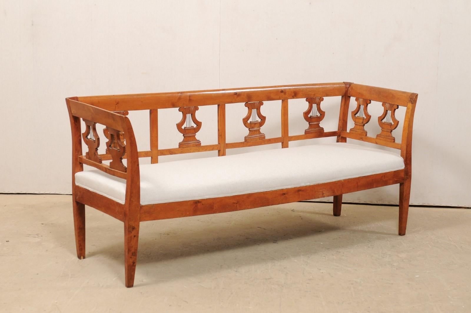 A Swedish neoclassical style carved Birchwood sofa bench from the mid-19th century. This antique settee from Sweden features a straight back rail atop a beautiful and widely spaced back splats of pierce-carved lyres (with metal pieces as cords). The