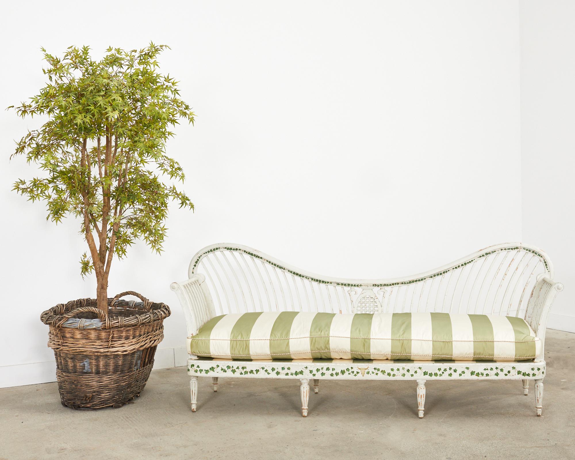 Grand Swedish painted pine daybed bench or settee made in the neoclassical taste. The pine frame features a gracefully curved back with spindles centered by a Greco-Roman urn form. Each side of the bench has scrolled arms. The piece is decorated
