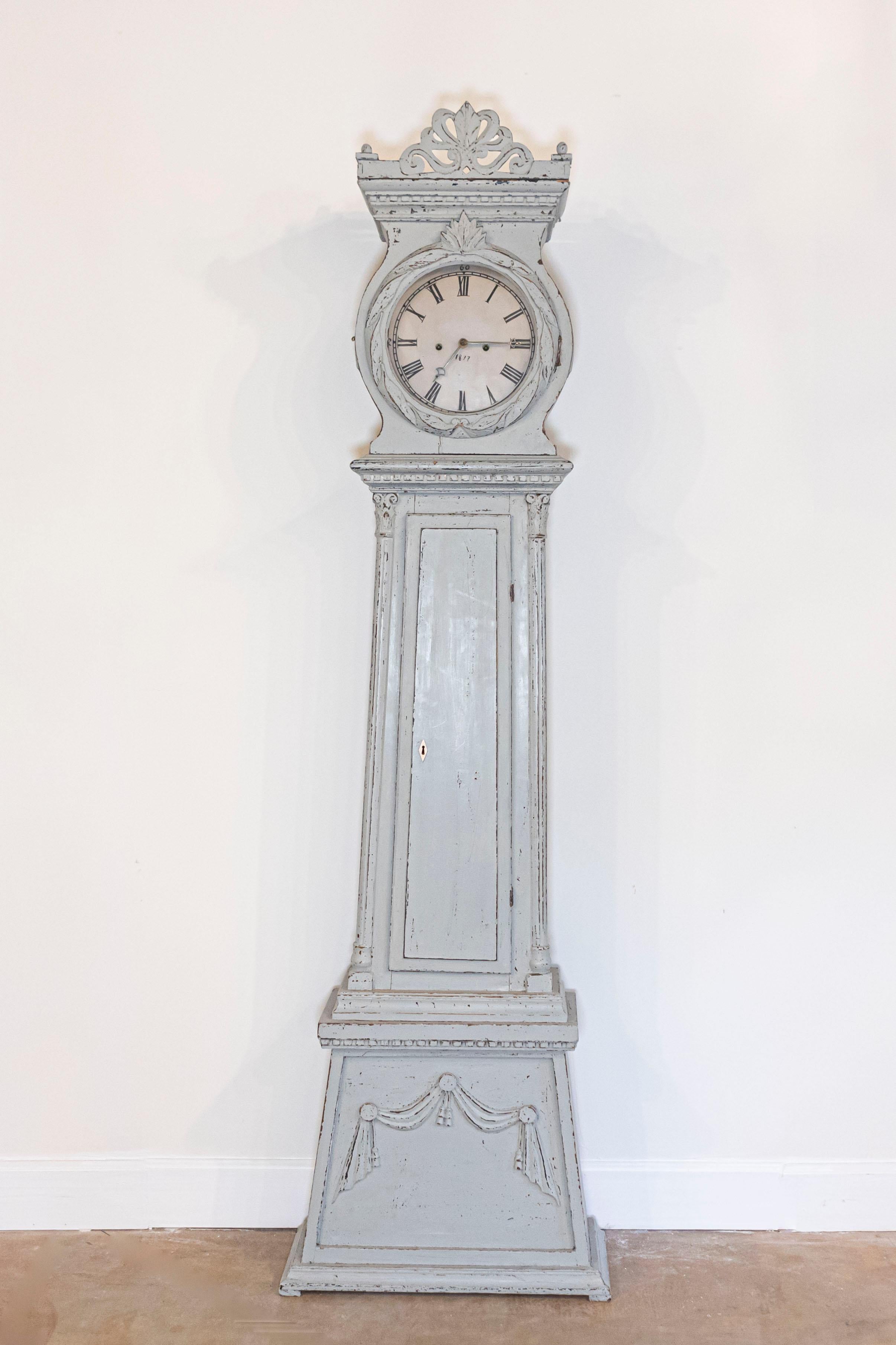 Horloge suédoise du début du 19e siècle, de style néoclassique, en bois peint, avec un cimier sculpté, une tête circulaire et un corps linéaire. Cette horloge grand-père suédoise en bois peint présente un écusson exquis, orné d'une palmette sculptée