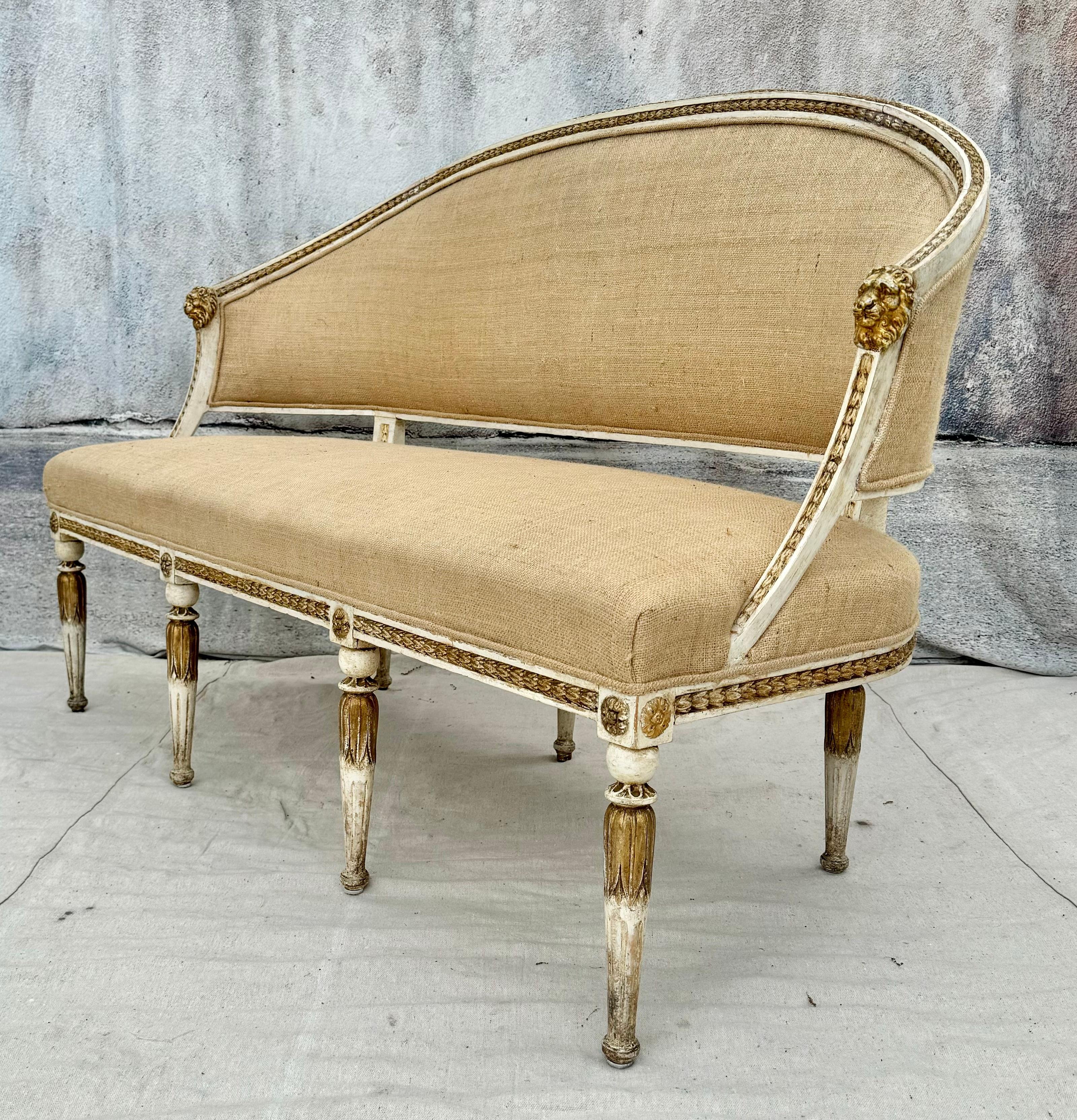 Beautiful cream painted Swedish neoclassical style giltwood upholstered settee. Settee has a curved back with gilt lion's head corners.  Features twisted rope gilt trim on arms and across back and across apron with gilt medallions atop each of the