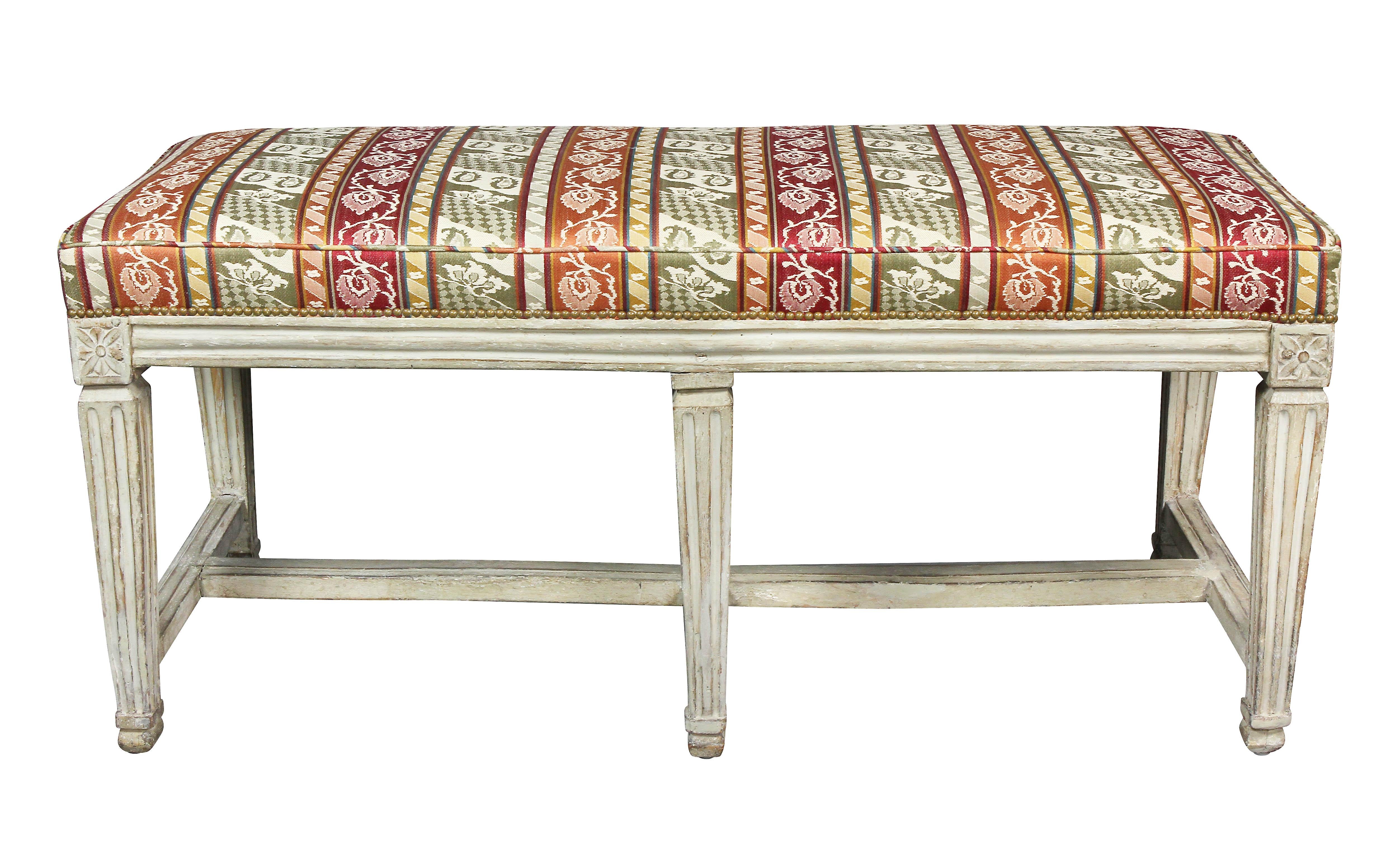 With rectangular upholstered seat over a frame with six tapered legs headed by paterae, joined by stretchers.