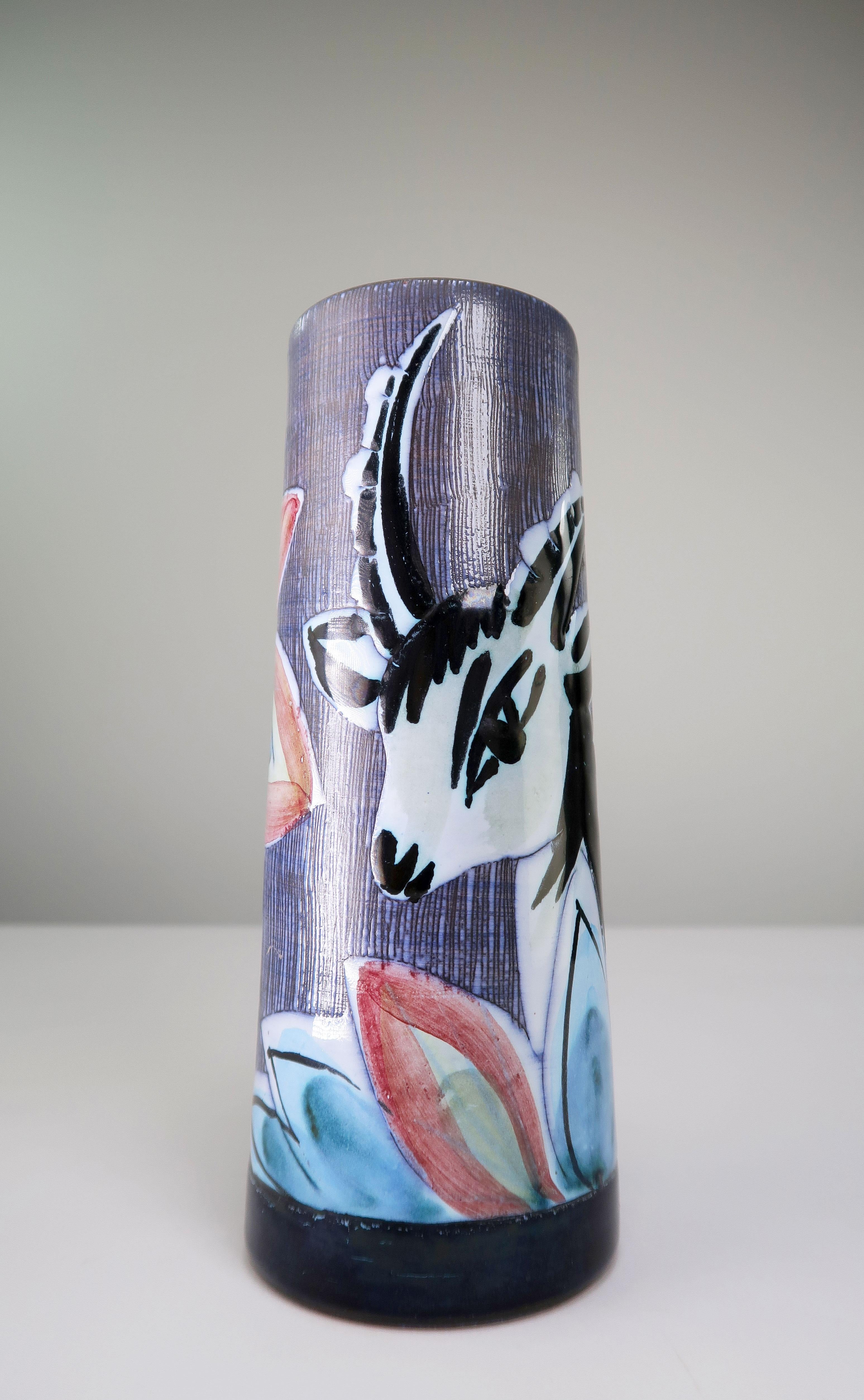 Hand-painted Swedish midcentury modern cylinder vase depicting the head of a black and white gazelle in wild growing flowers in blue, rose, green and yellow colors. Sgraffito technique on the background of the image. White glaze on the inside and