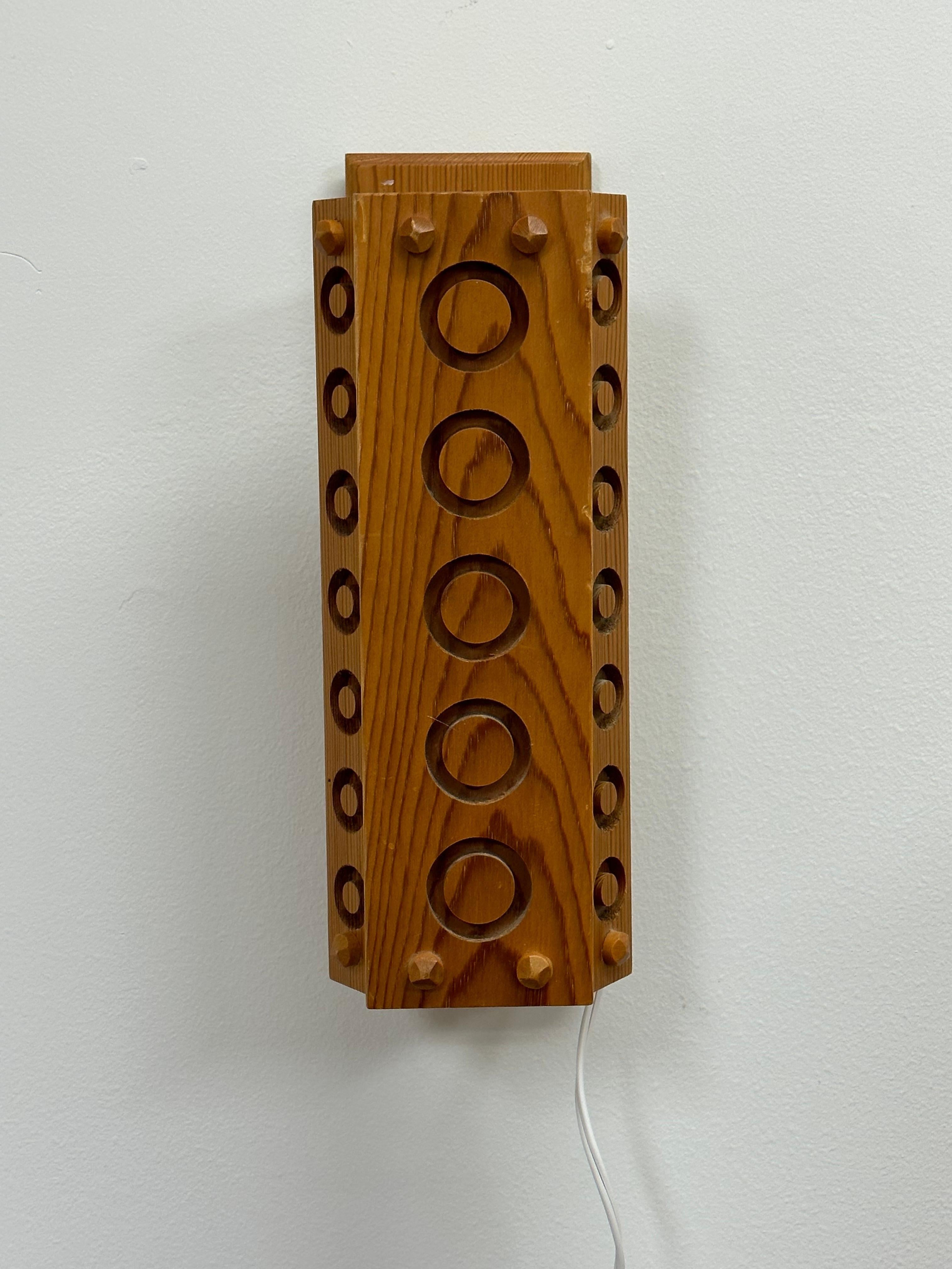 Eine wunderschöne schwedische Wandleuchte aus Kiefernholz mit kreisförmig gefrästen Mustern. Mit einem schwenkbaren Schirm, der sich zu beiden Seiten ein wenig bewegen lässt, kann die Leuchte sowohl horizontal als auch vertikal montiert werden.