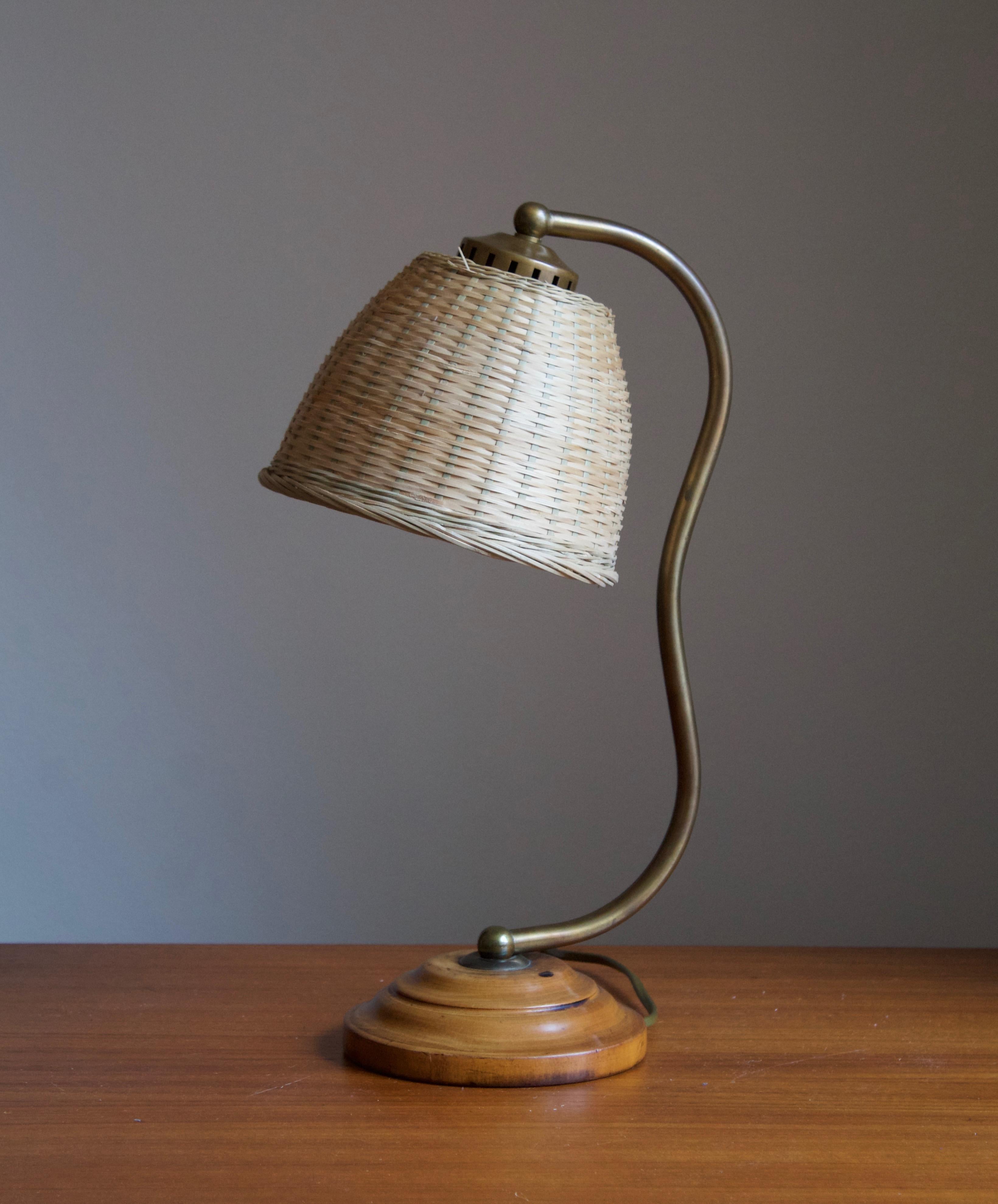 A table lamp, designed and produced in Sweden, circa 1930s. Features an organic brass rod on a wooden base. Assorted vintage rattan lampshade.