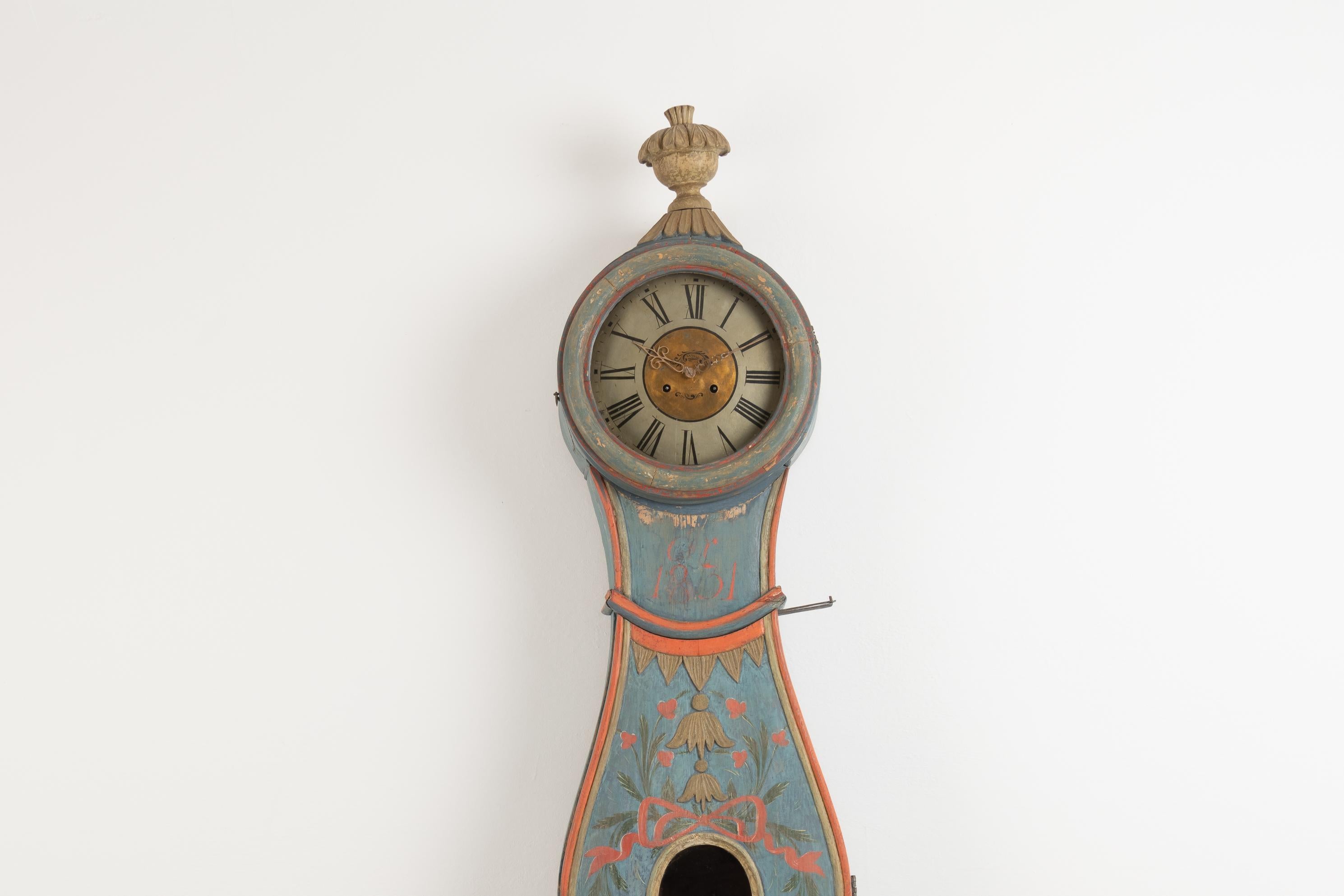 Swedish long case clock with hand scraped to original blue paint. The clock shows influences from the rococo period with the curved case. Hand carved decoration in wood at the top of the head. The clock is from the municipality Ljusdal in the