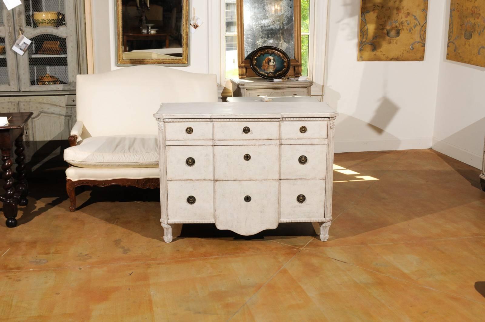 A Swedish painted breakfront three-drawer commode from late 19th century Stockholm, with dentil molding, carved rosettes and tapered feet. This Swedish painted commode features a slightly raised rectangular top with canted corners in the front