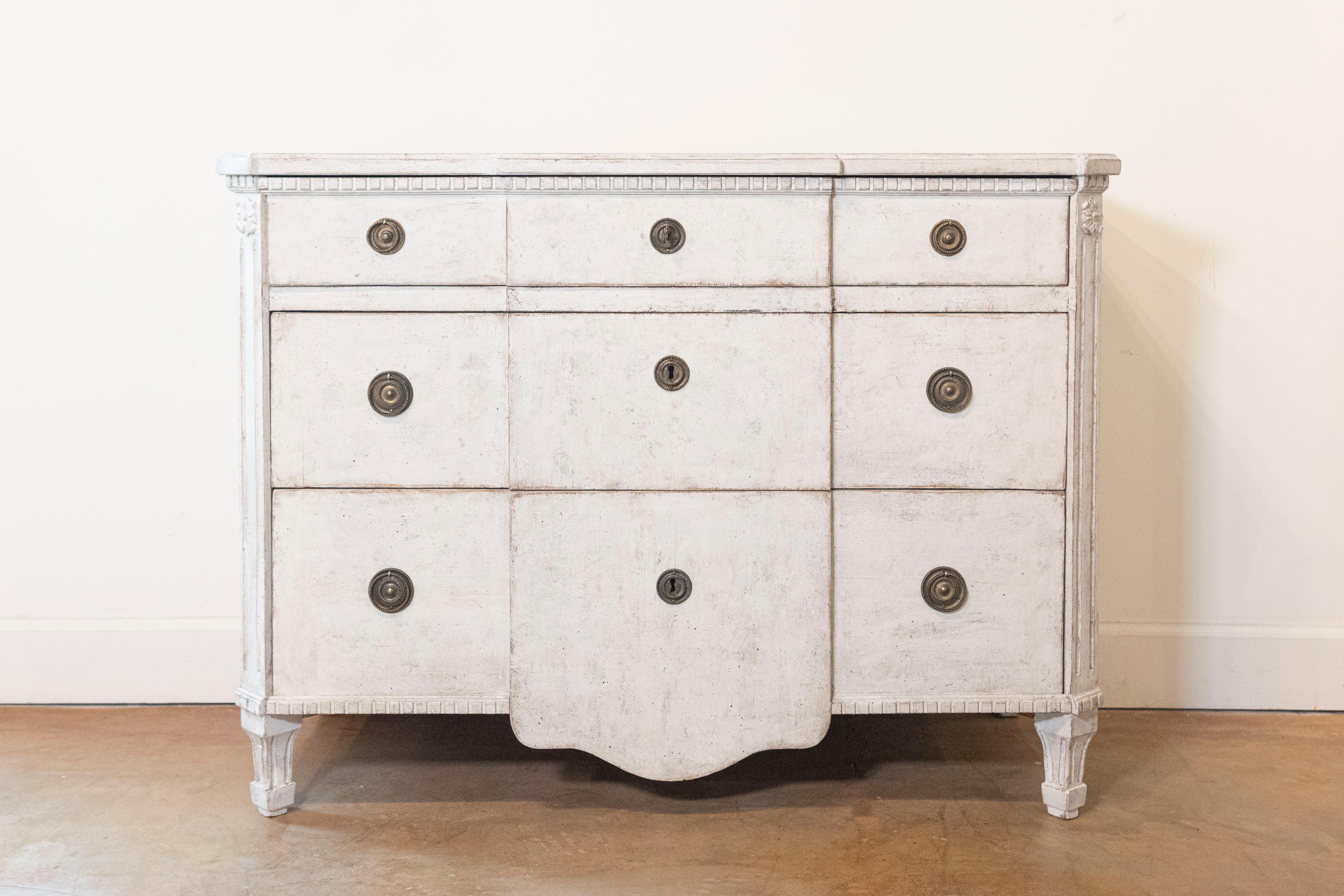 A Swedish painted breakfront three-drawer commode from late 19th century Stockholm, with dentil molding, carved rosettes and tapered feet. This Swedish painted commode features a slightly raised rectangular top with canted corners in the front