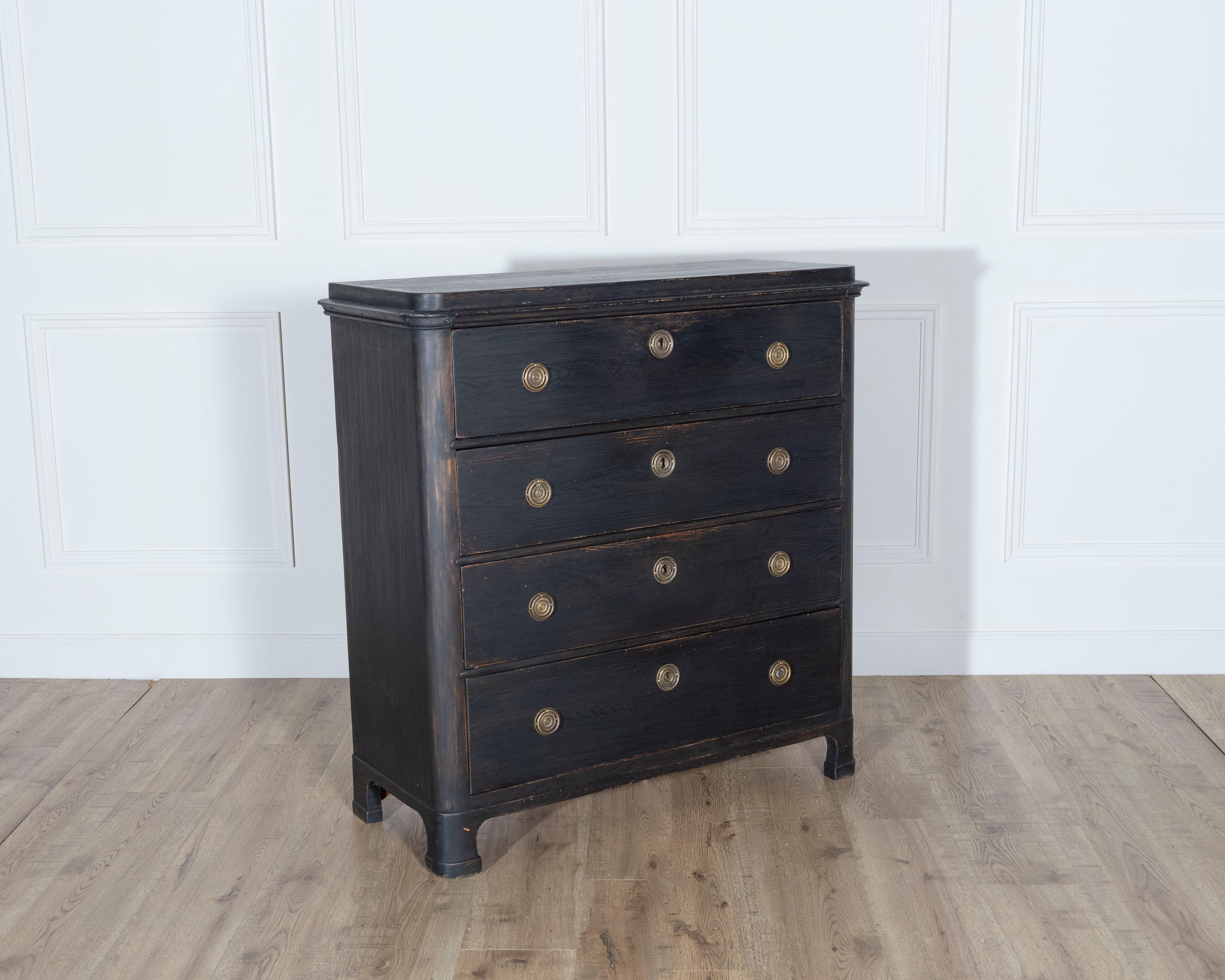 A handsome Swedish chest of drawers dating to approximately 1860, painted in a deep, subtly distressed black that enhances its classical form and rich texture. This chest features five spacious drawers, each adorned with original circular brass