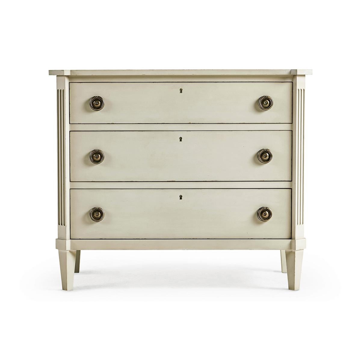 Swedish painted commode, this neo-classic painted commode in an antiqued white London mist finish with three long lockable drawers, canted corners with fluted stiles, and brass ring pull handles on square tapered legs. 

Dimensions: 38