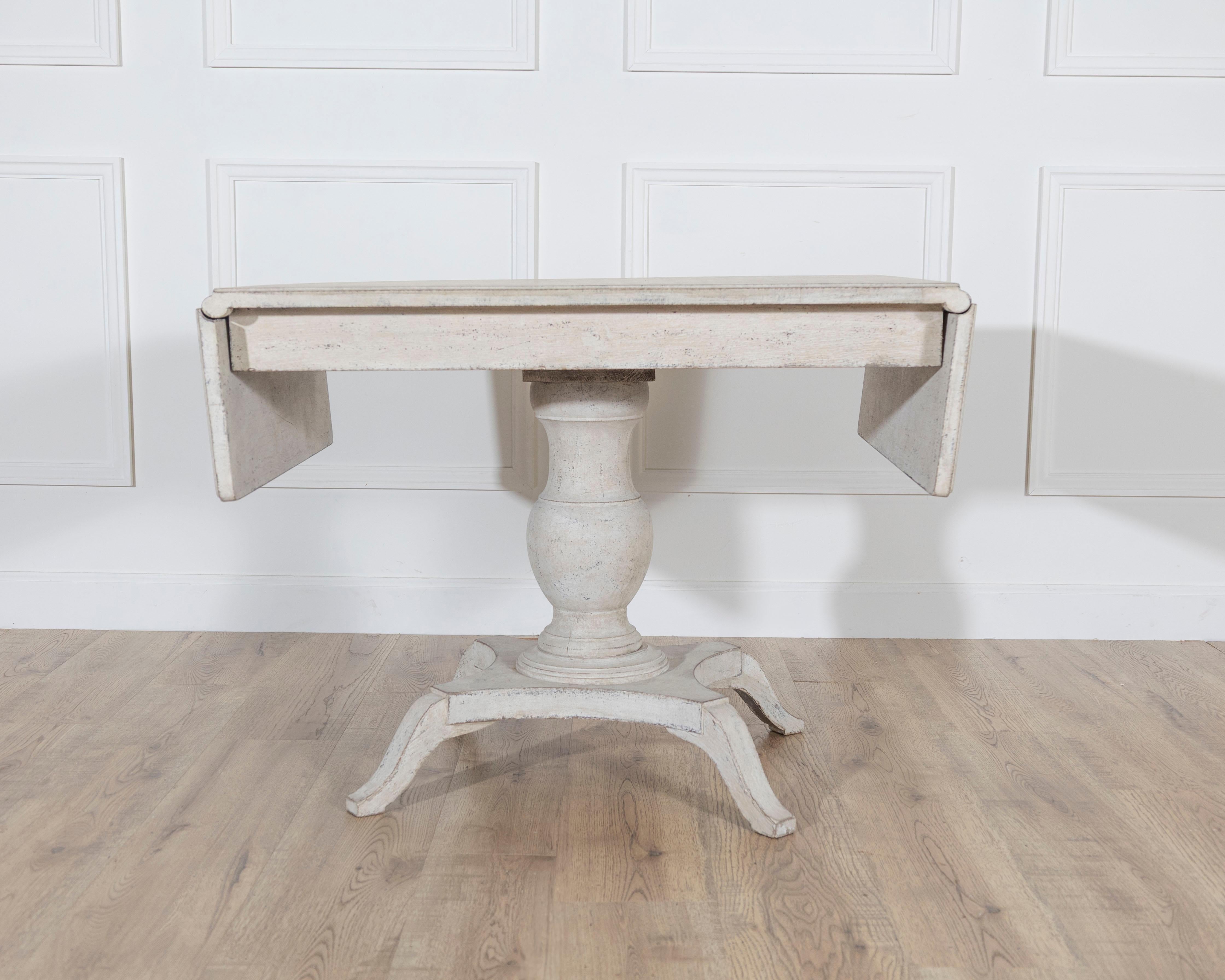 A charming Swedish table from around 1880, designed with two drop-leaf flaps that allow the piece to expand or contract as needed. The table is supported by a central turned pedestal column resting on four gracefully shaped legs, a form that
