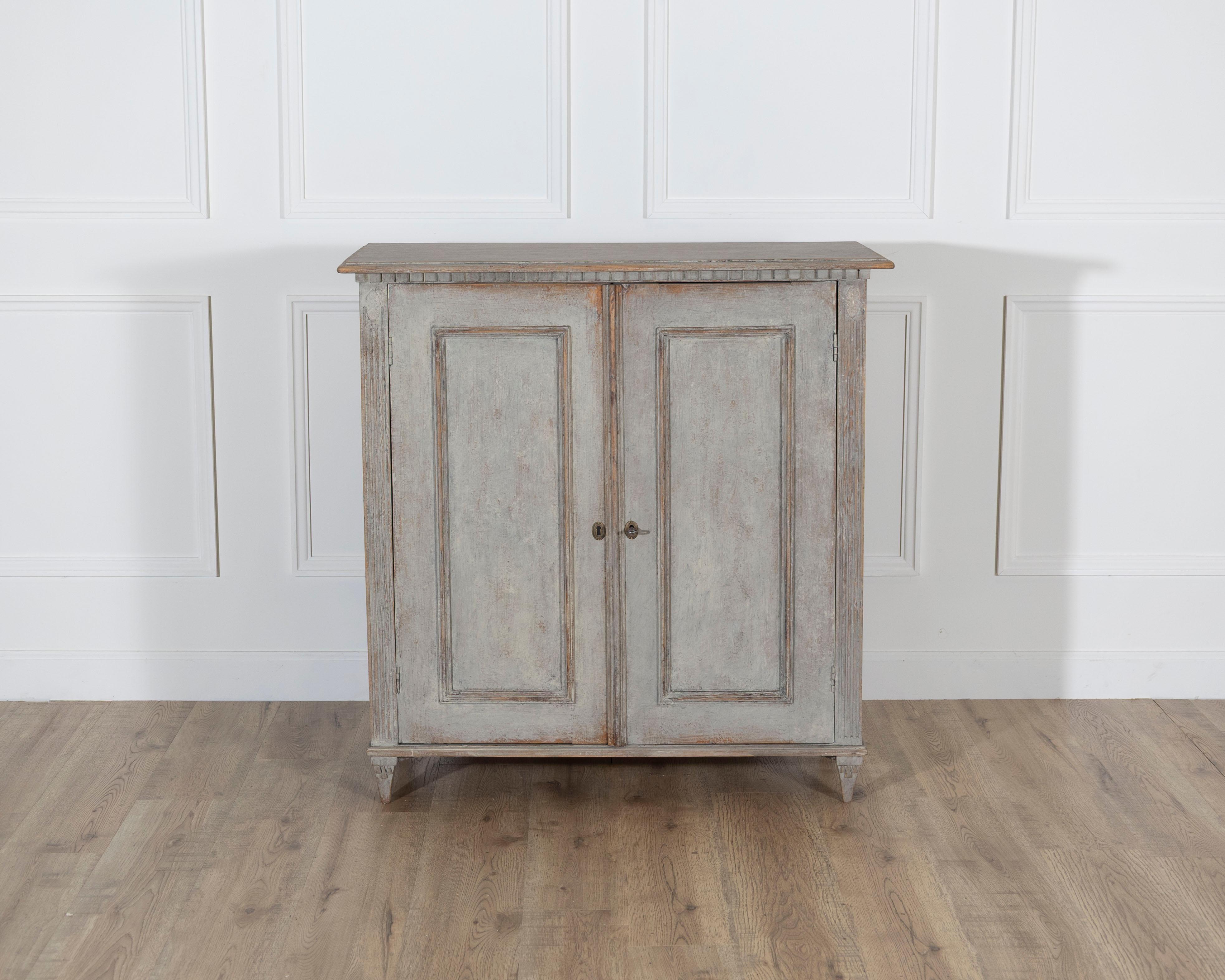 A refined Swedish sideboard from the mid-19th century, painted in a soft grey tone that enhances its quiet elegance and timeless form. The rectangular top is framed by a decorative dentil frieze, a neoclassical detail typical of Gustavian influence.