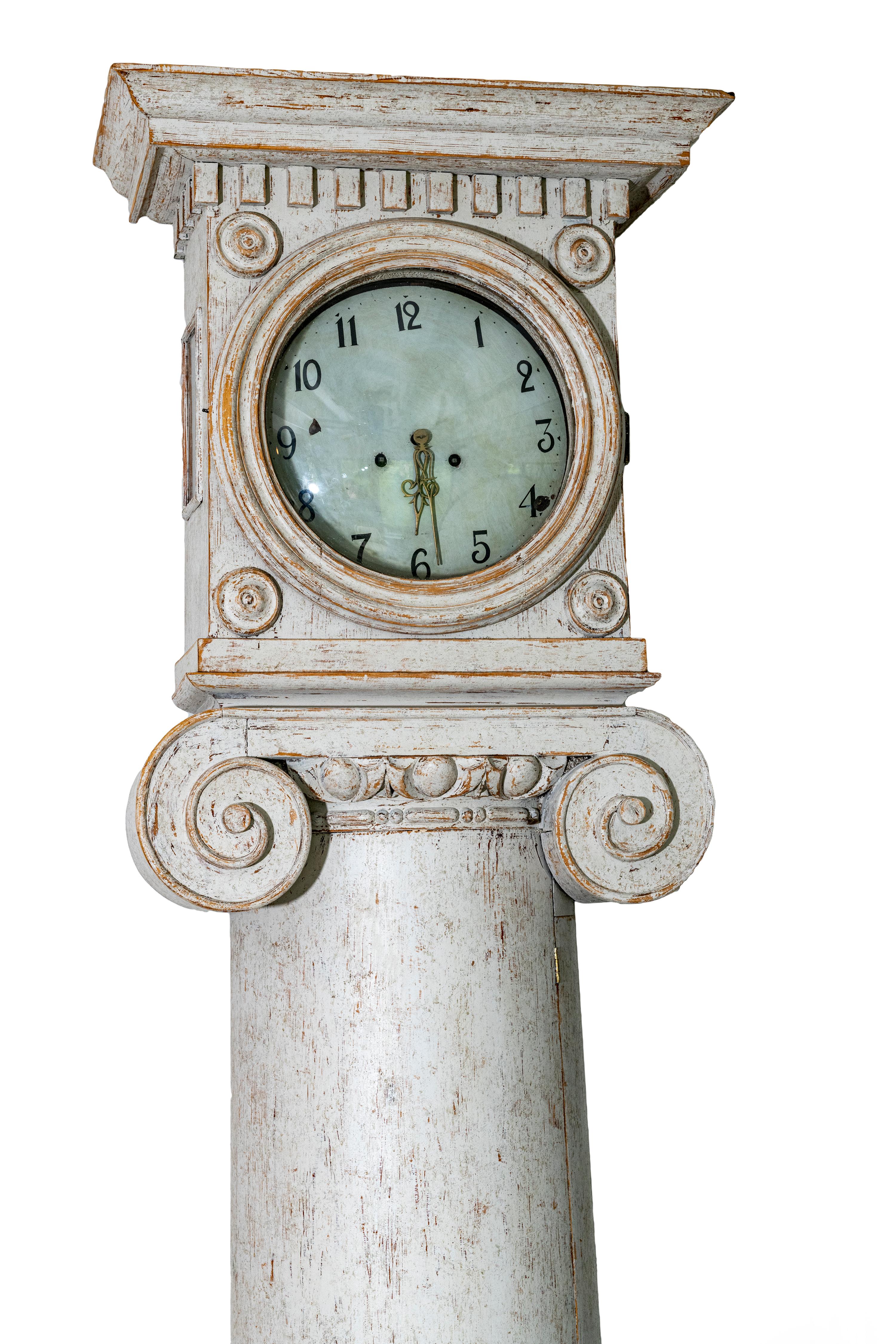 A Swedish painted tall case column clock from the late 18th century.

There are two decorative brass clock hands.

The face is secured behind a single hinged glass door. The top of the clock has a carved ionic column and carved dental