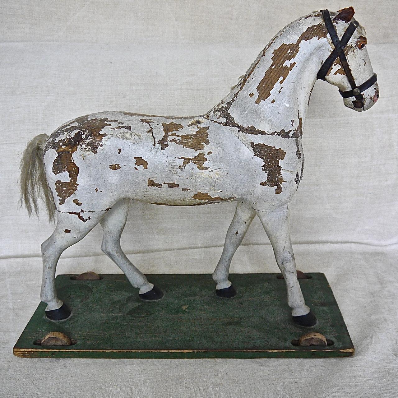 Beautiful Swedish 19th century painted carved wooden toy horse with a very elegant stance. Painted white and mounted on a green painted base with wooden wheels. With leather ears and harness and a combed wool tail and the remains of a wool mane on