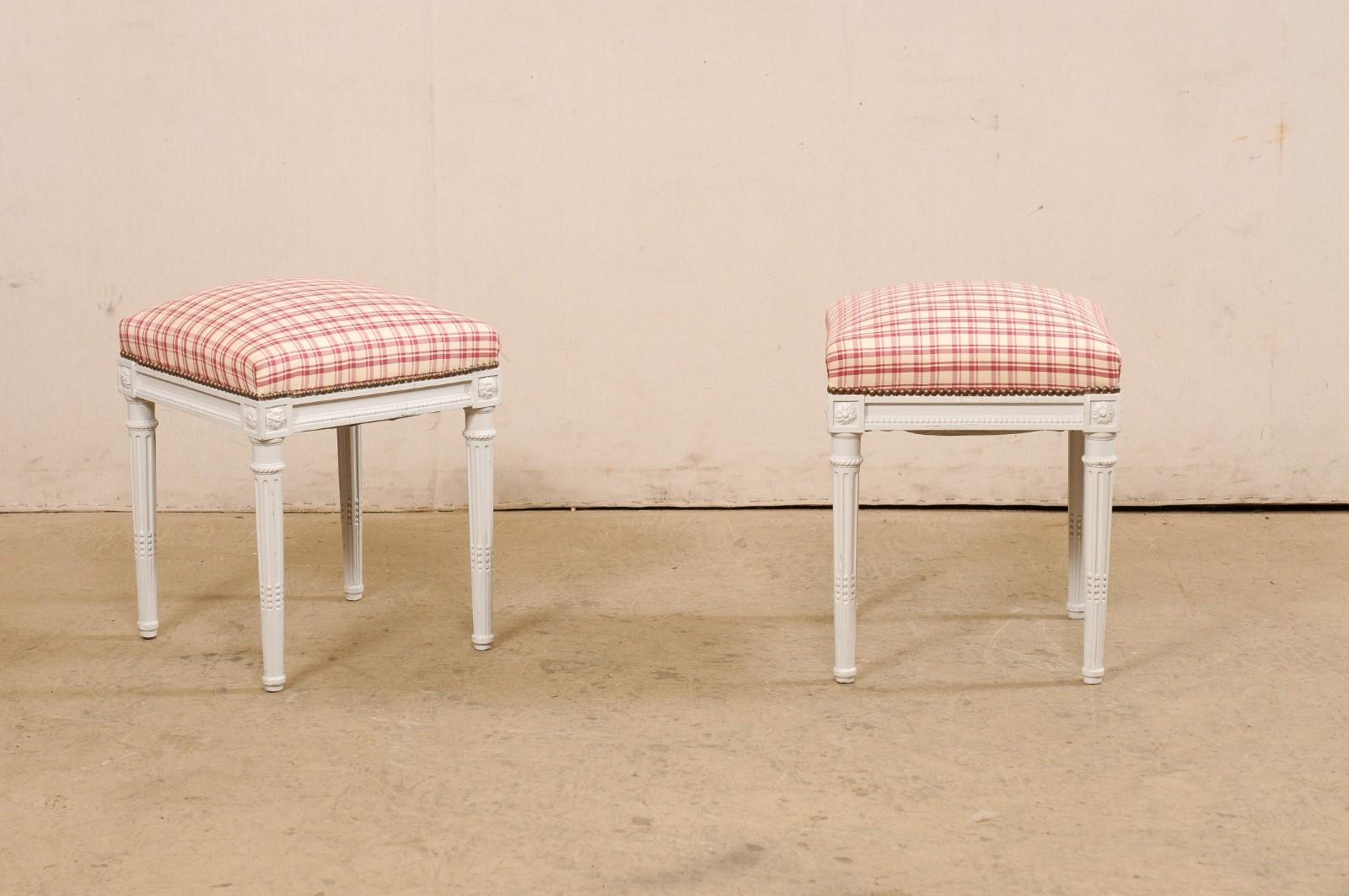 A Swedish pair of painted wood stools with upholstered seats from the mid 20th century. These vintage stools from Sweden feature squared upholstered seats which sit without an apron that has linear molding, accented with a petite bead accent trim,