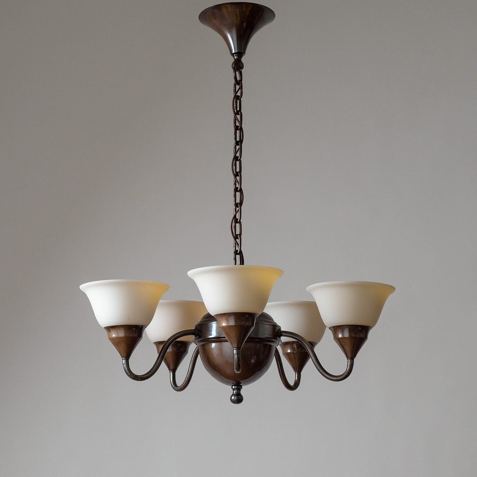 Swedish patinated brass chandelier from the 1920s. The satin glass diffusers are enameled on the inside in bright yellow/orange (each a slightly different nuance) for a warm glow when lit. Very good original condition with a light patina. Five