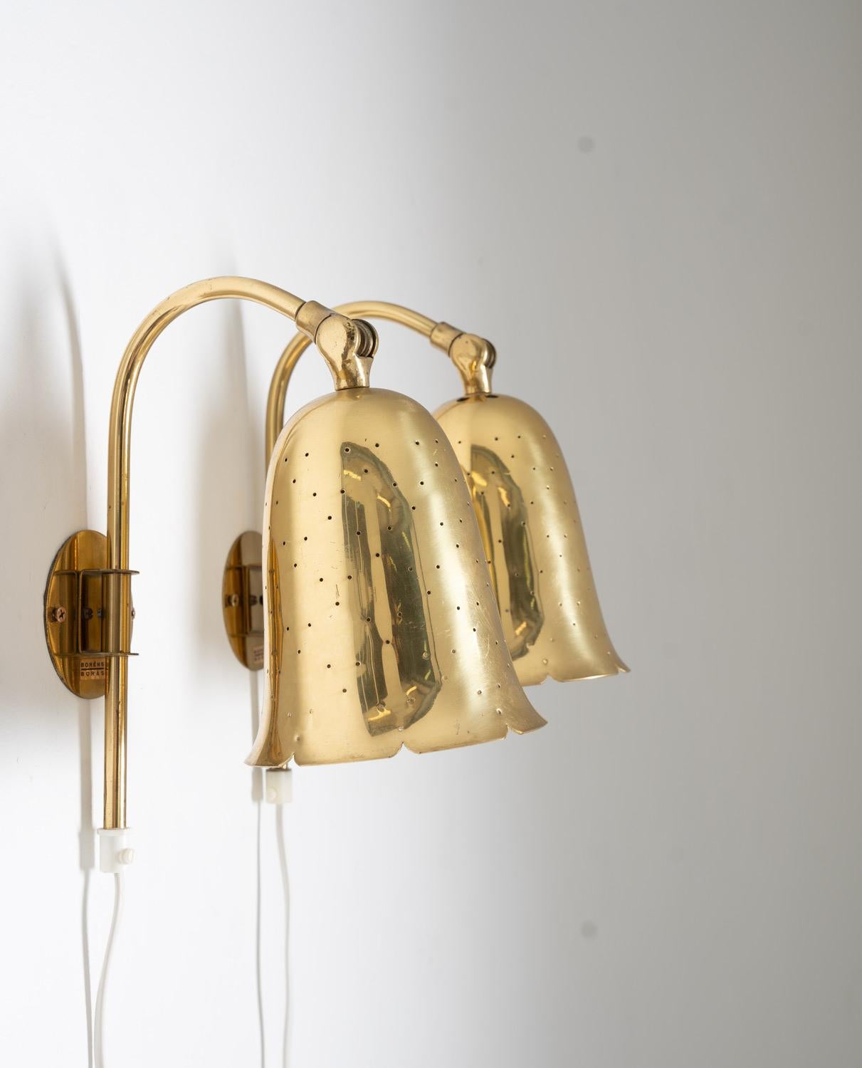 This charming pair of Boréns wall lamps was produced in Sweden during the 1960s. The lamps have a distinctive design, featuring brass clock-shaped shades with perforations. One notable feature is their adjustable angle, allowing you to direct the