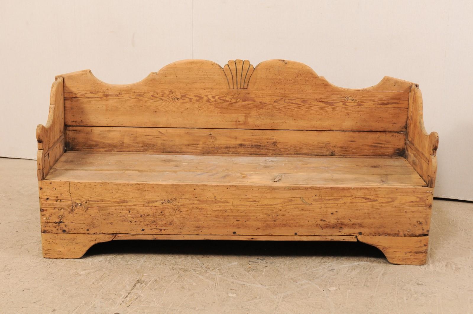 A Swedish period Gustavian wood sofa bench from the early 19th century. This antique wood bench from Sweden features a high back with nicely scalloped back rail with shell carved at centre, high and curvy side arms, a thick skirt, and is raised upon