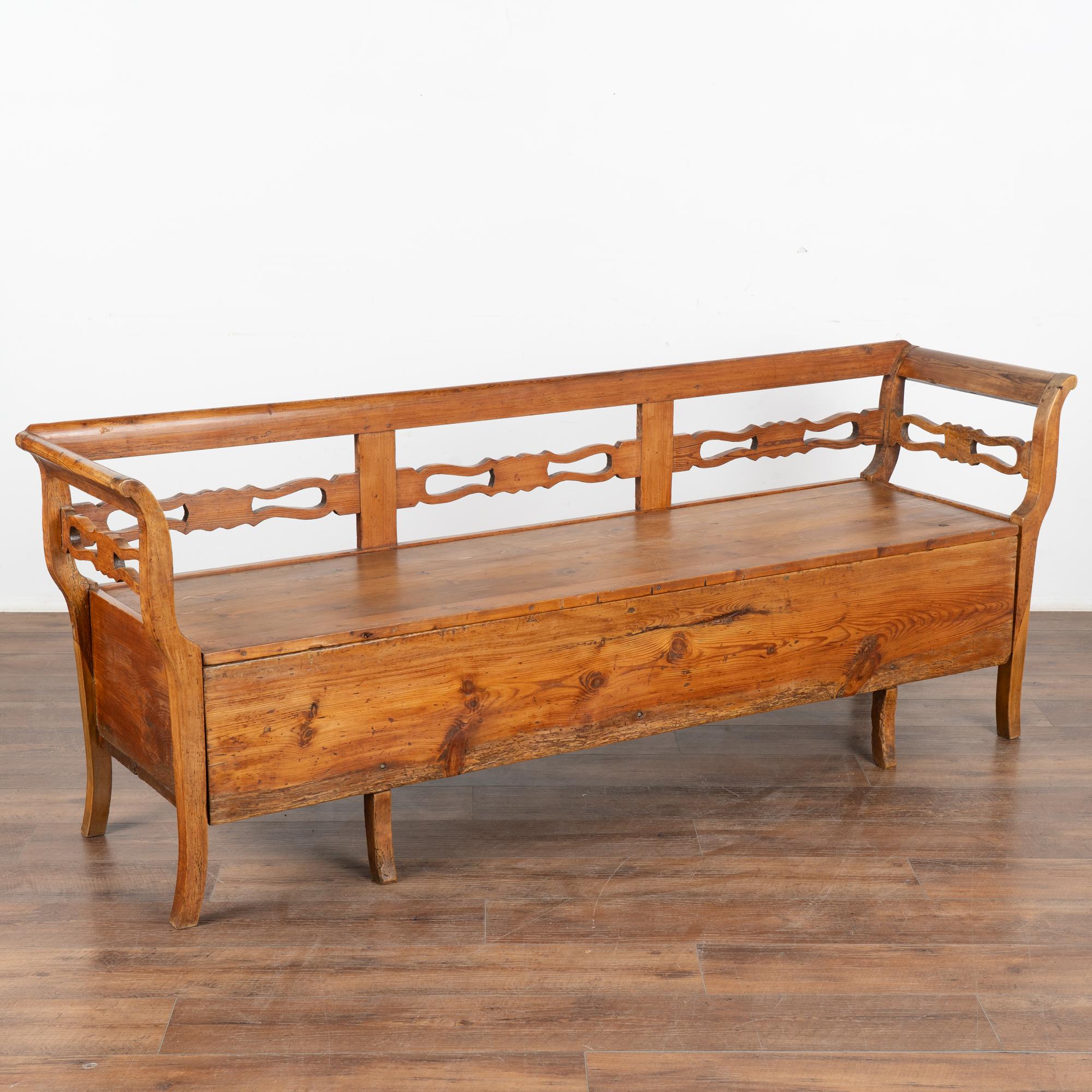The years of use have deepened the warm patina of the pine, aging gracefully through the years. The decorative carving along the back and arms add to its appeal.
Notice the seat is hinged, creating great storage space for items that need to be