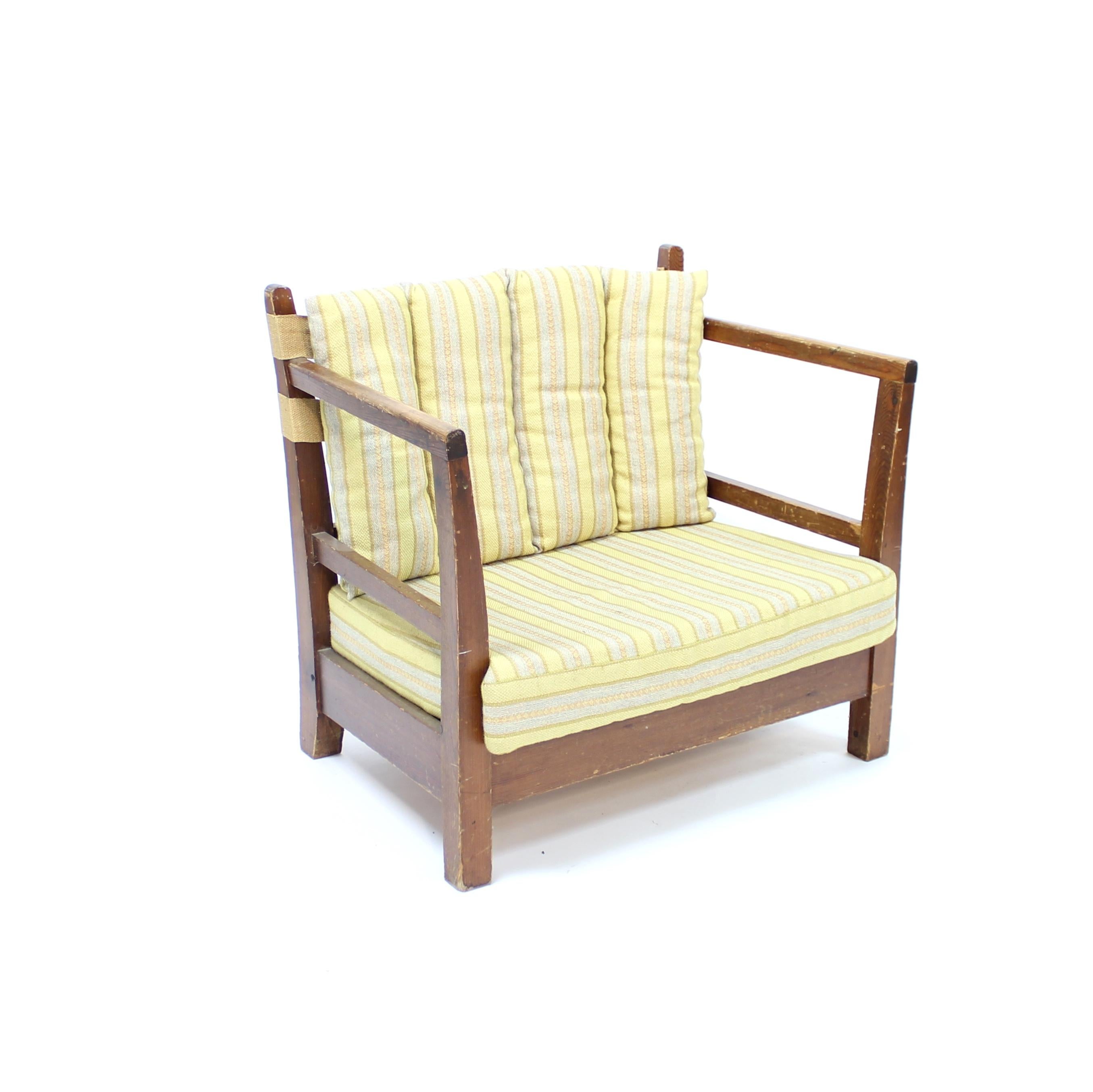 Tumbona de pino teñido a la manera de Axel Einar Hjorth, fabricada en Suecia en la década de 1930. Cojín de asiento y respaldo con tela original a rayas con tonos amarillos y grises. Los cojines del respaldo están sujetos por dos tiras de cincha de