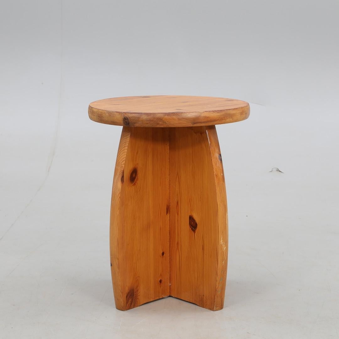 Grazioso sgabello rustico in pino realizzato in Svezia negli anni '70. Questo pezzo è caratterizzato da una spessa seduta rotonda e da gambe scultoree che si intersecano, mettendo in mostra le venature naturali, i nodi e le calde tonalità del miele