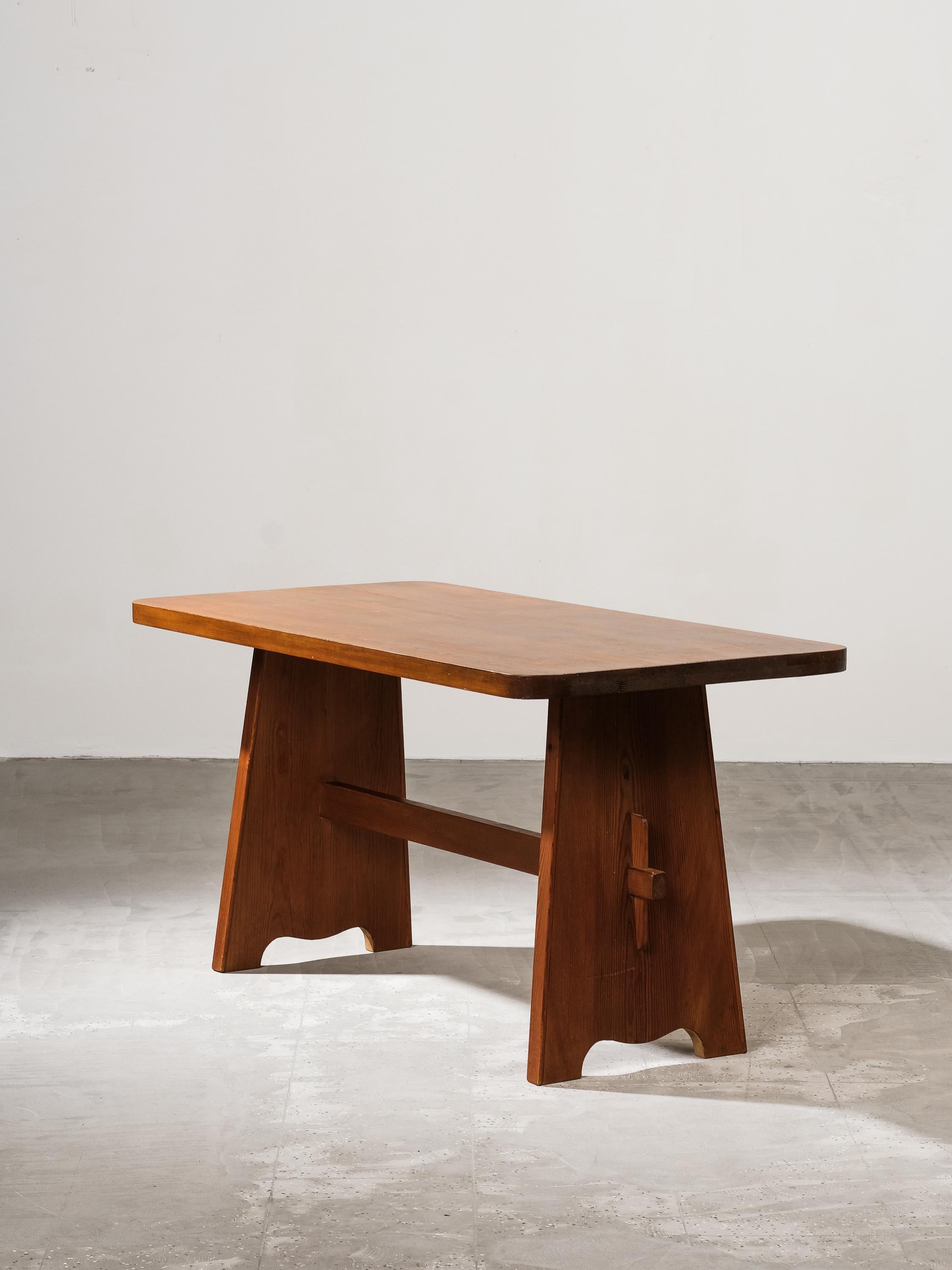 This Swedish dining table from the 1940s exemplifies the rustic elegance and functional charm associated with the work of Carl Malmsten, Göran Malmvall, and Axel Einar Hjorth. Crafted from solid pine, the table features a rectangular top with softly