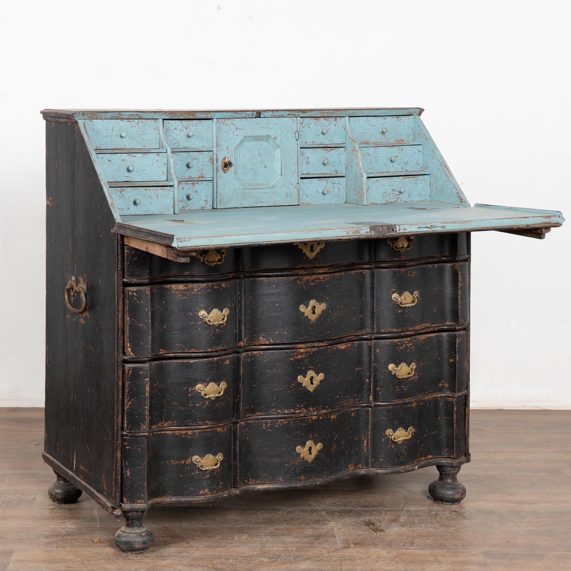 Questa segretaria in stile rococò presenta il monogramma KNS e la data del 1778 lungo il piano anteriore della scrivania e poggia su piedini a bacchetta.
Gli scenografici cassetti a serpentina con frontale sinuoso e tiranti in ottone aggiungono un