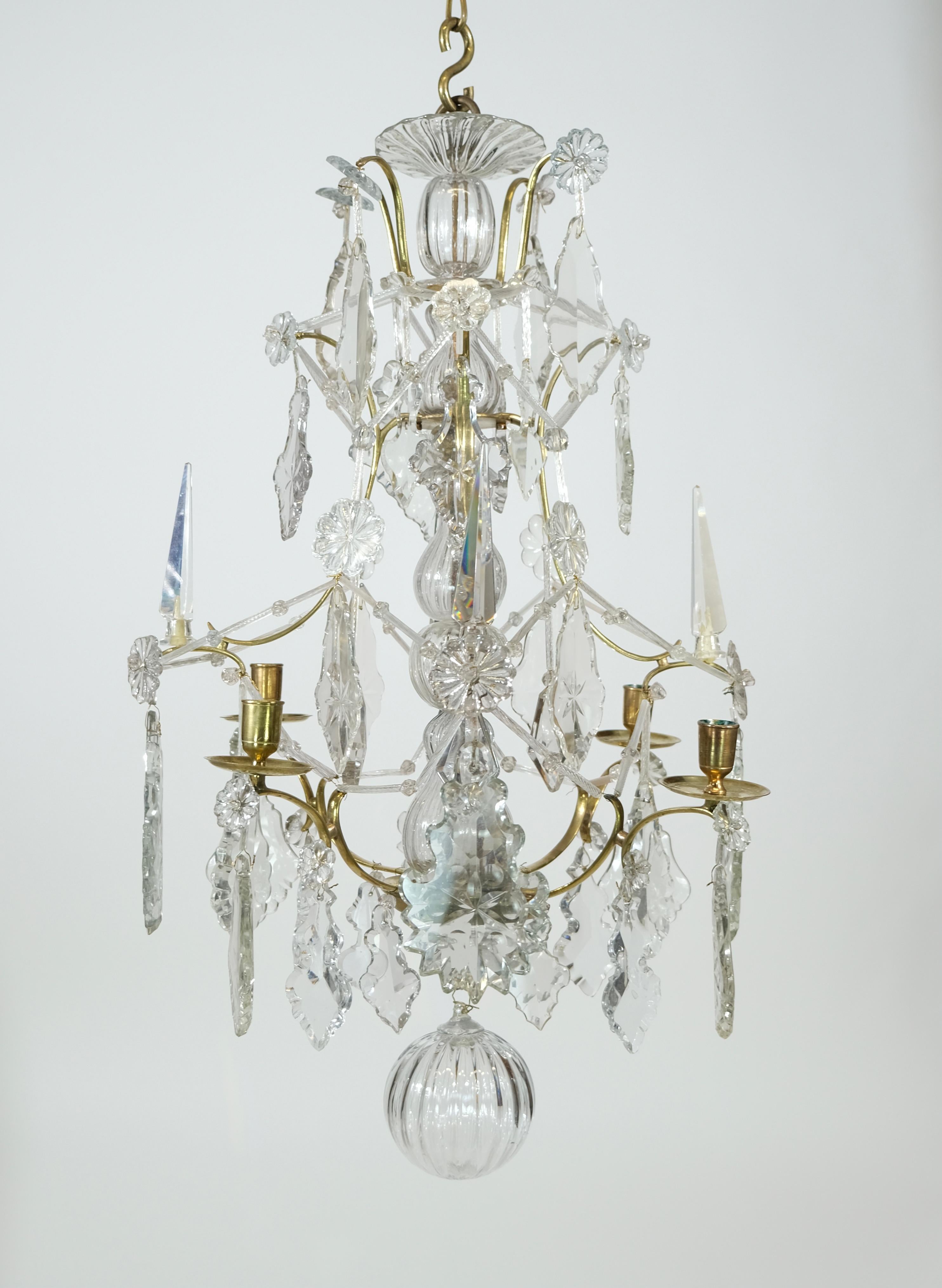 A small Swedish Rococo brass and cut-glass four-light chandelier, 18th century.
The brass cage hung with cut-glass leaf-shaped pendants and other shapes. The center stem dressed with blown glass pieces ending below with a blown glass bowl.
The