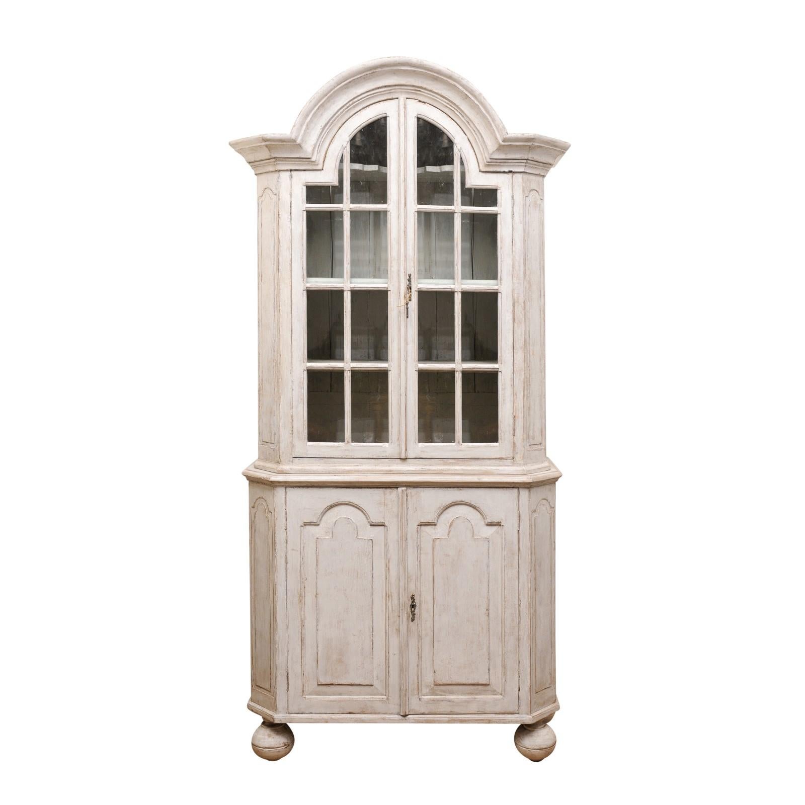 A Swedish Rococo period two-part vitrine cabinet from the mid 18th century, with bonnet pediment, glass doors and ball feet. Created in Sweden during the third quarter of the 18th century, this Rococo cabinet features a large bonnet top sitting
