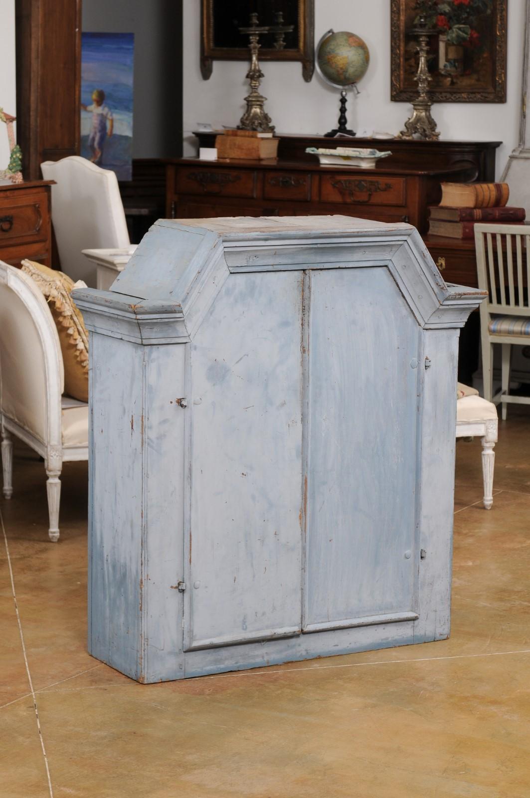 A Swedish Rococo style painted wood wall cabinet from the 19th century, with angular pediment, distressed grey paint, molded accents and two doors. Created in Sweden during the 19th century, this Rococo style wall cabinet features an angular