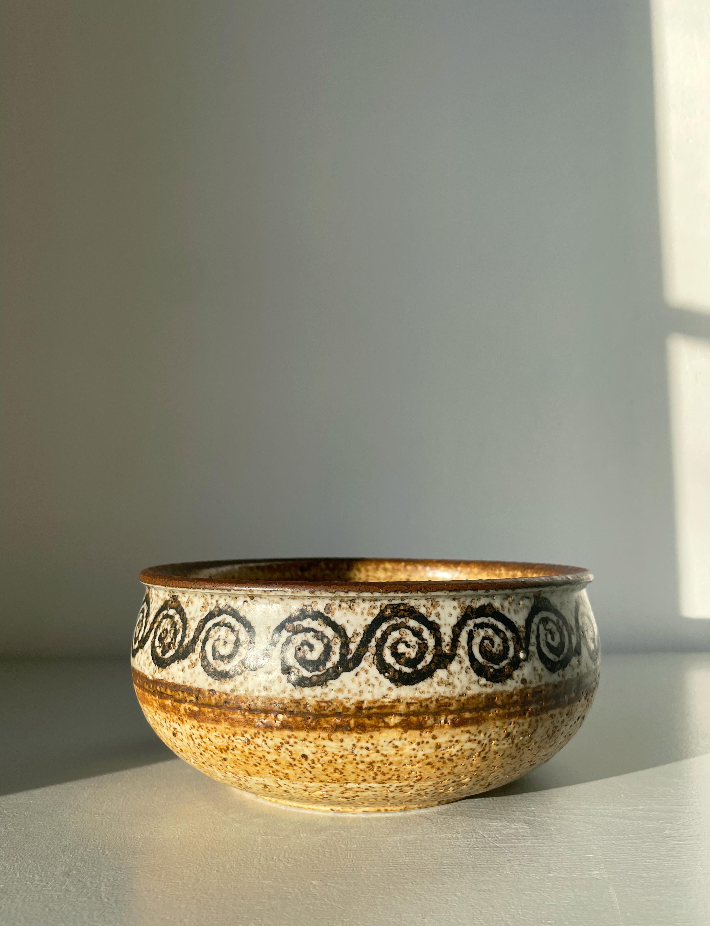 Vintage stoneware decorative bowl designed by the artist group Drejargruppen for Rörstrand in 1974. Glazed in sand, terracotta, parchment and brown colors with black hand painted circular decor around the top edge. Signed under base. Beautiful