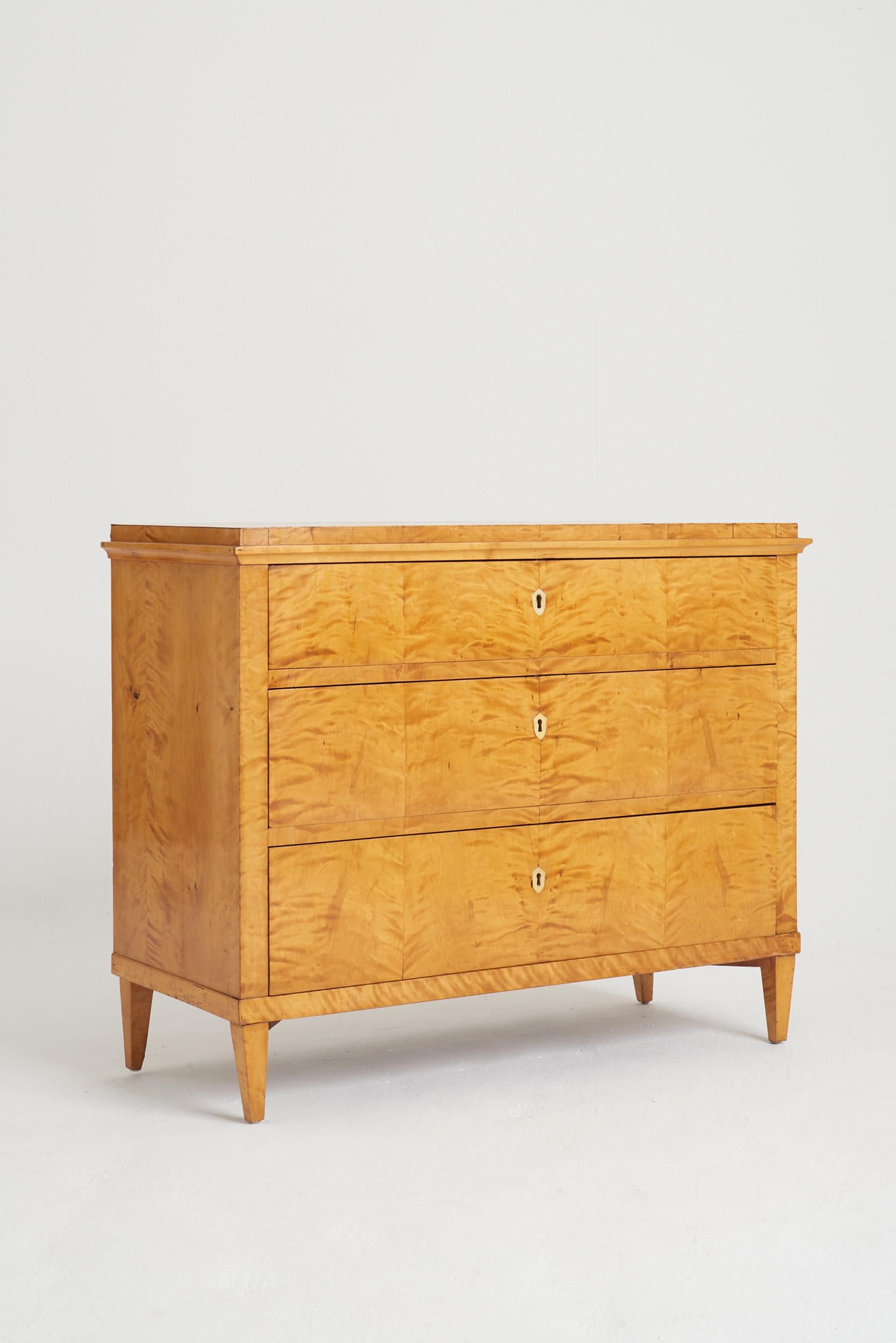 A satin birch chest of drawers, the top drawer revealing a fitted secretaire, with bone knobs and escutcheon key holes.
Sweden, Mid-19th Century.