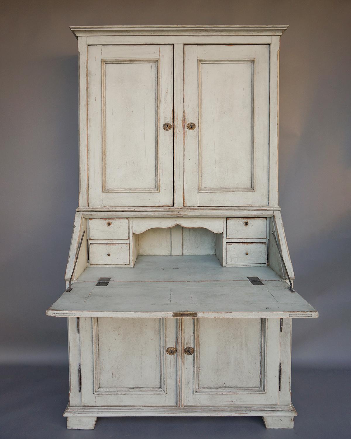 Two-part secretary, Sweden circa 1840, with paneled doors top and bottom and matching panels on the slant front. The upper section has a simple molded cornice and two locking interior compartments, each with a pair of fixed shelves. The left side